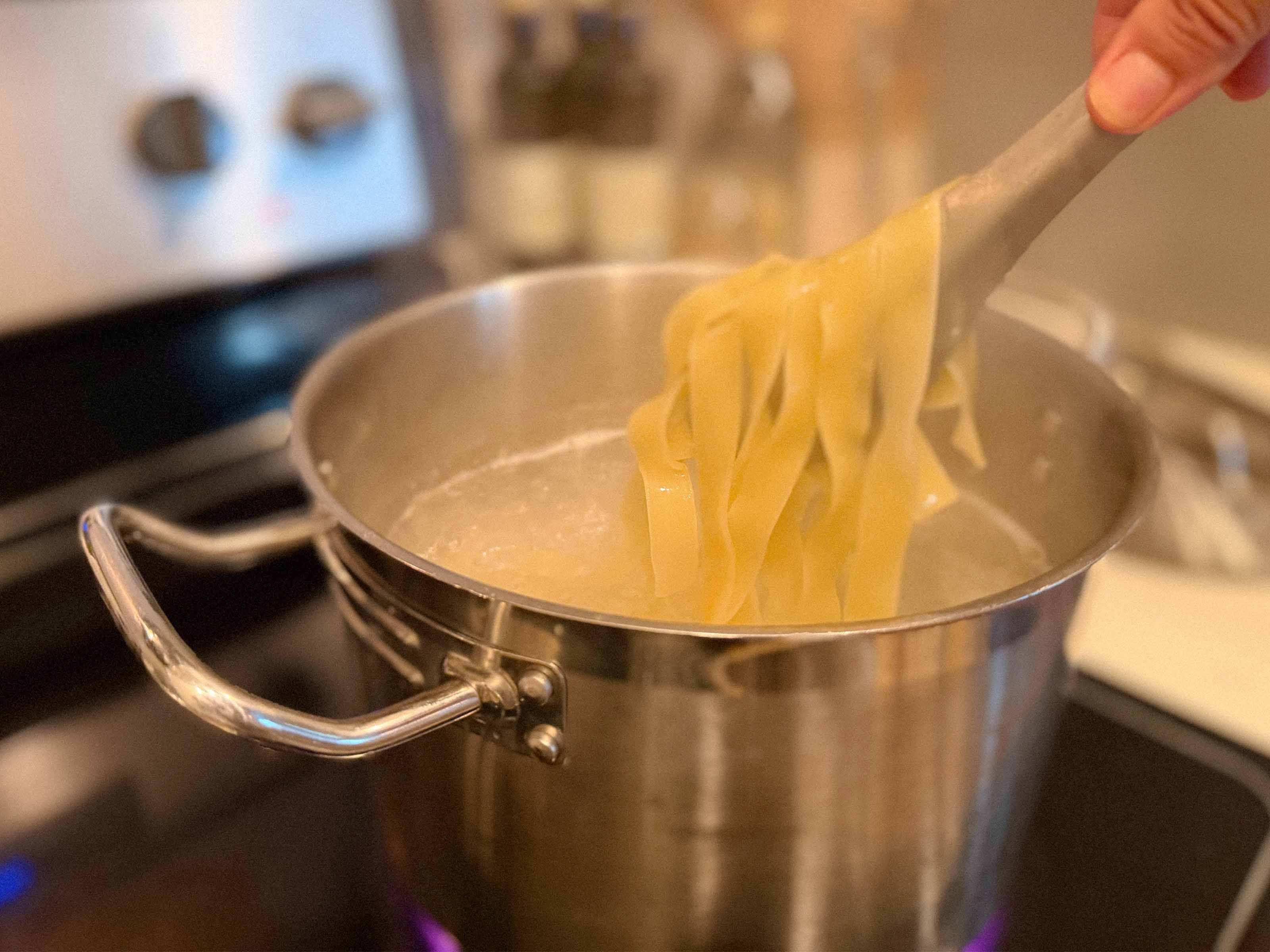 Cooking fresh pasta in a stainless steel pot using kitchen tongs.