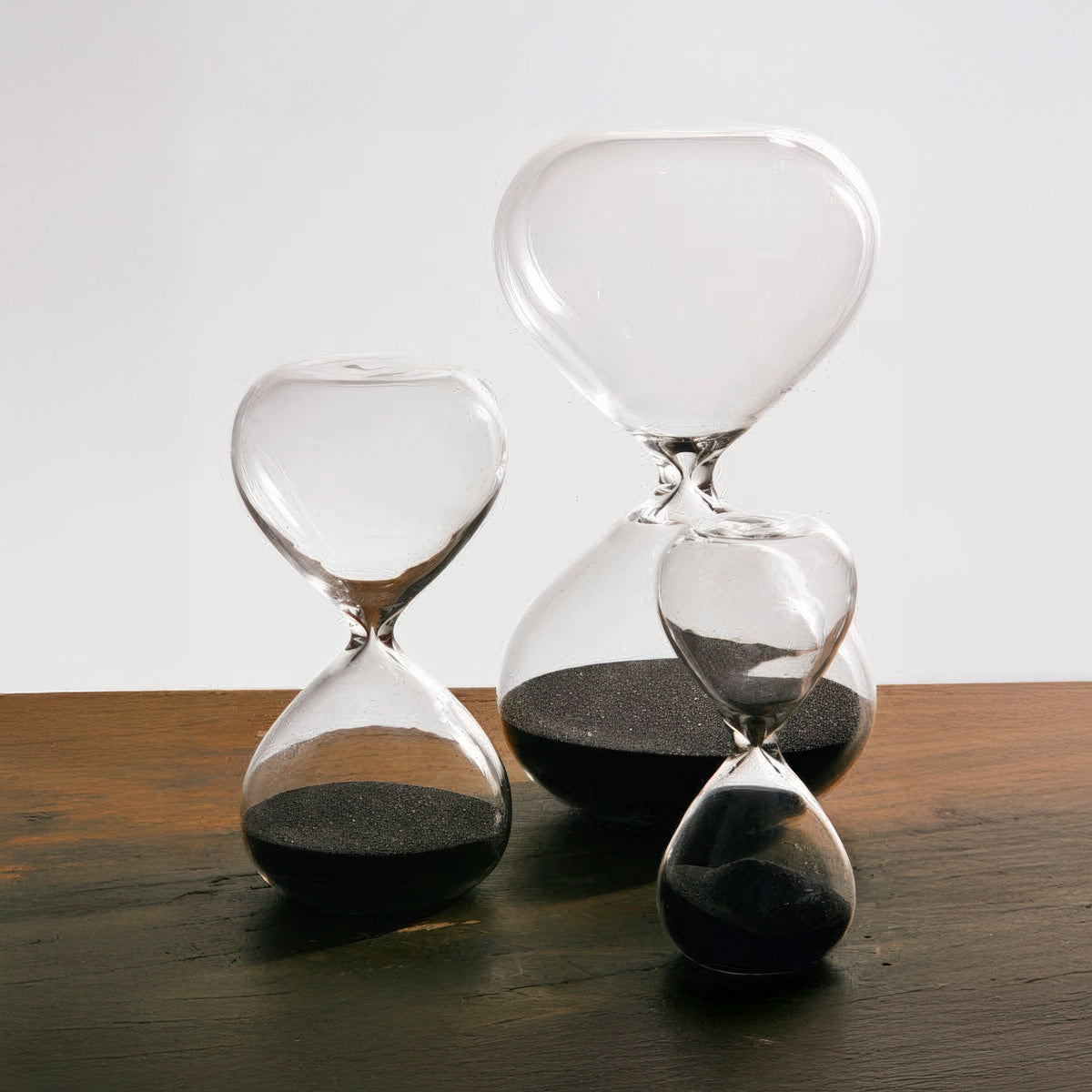Three hourglasses with sand running through on a wooden surface.