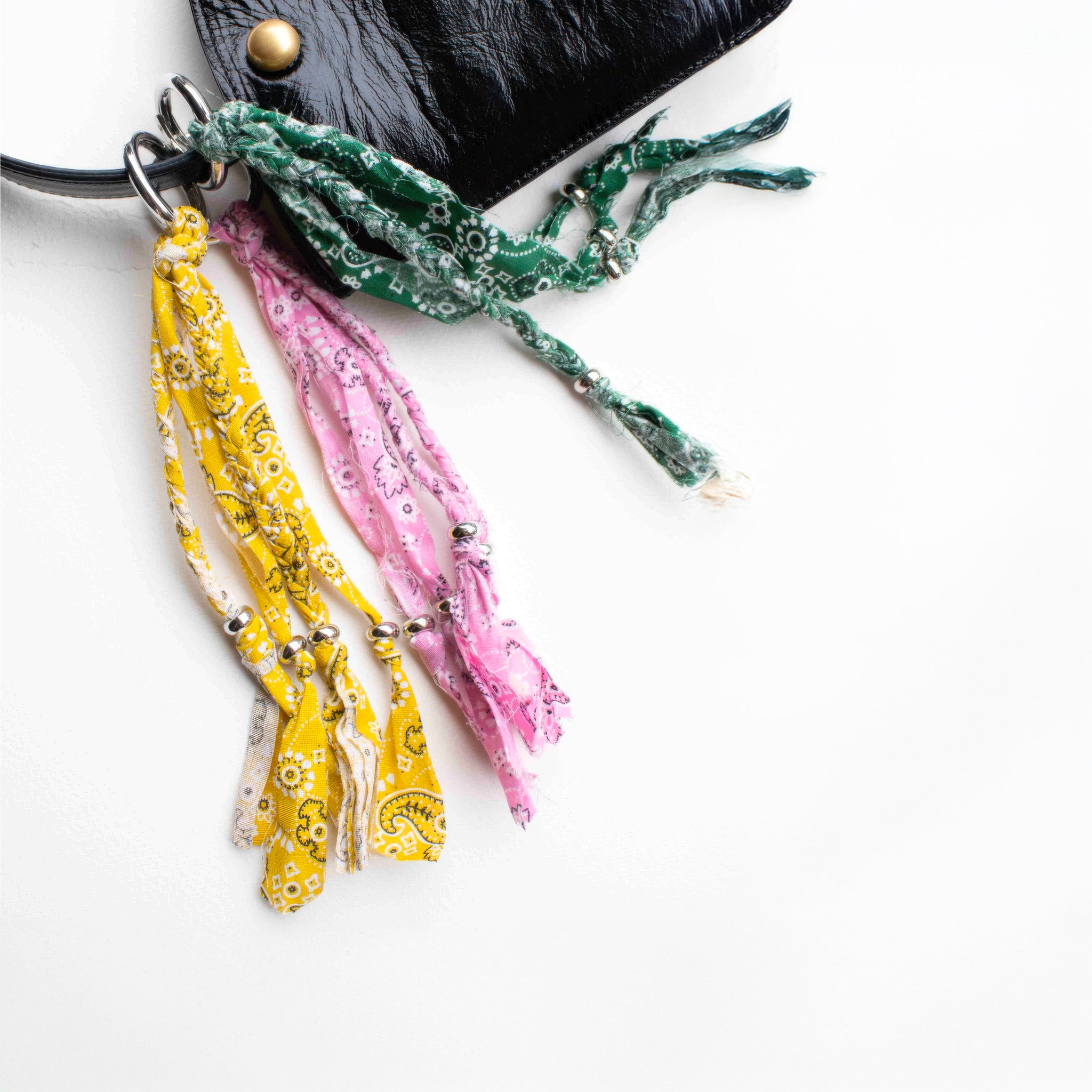 Colorful tassel keychains or bag charms with mustard, pink, and green bandana tassels on a white background