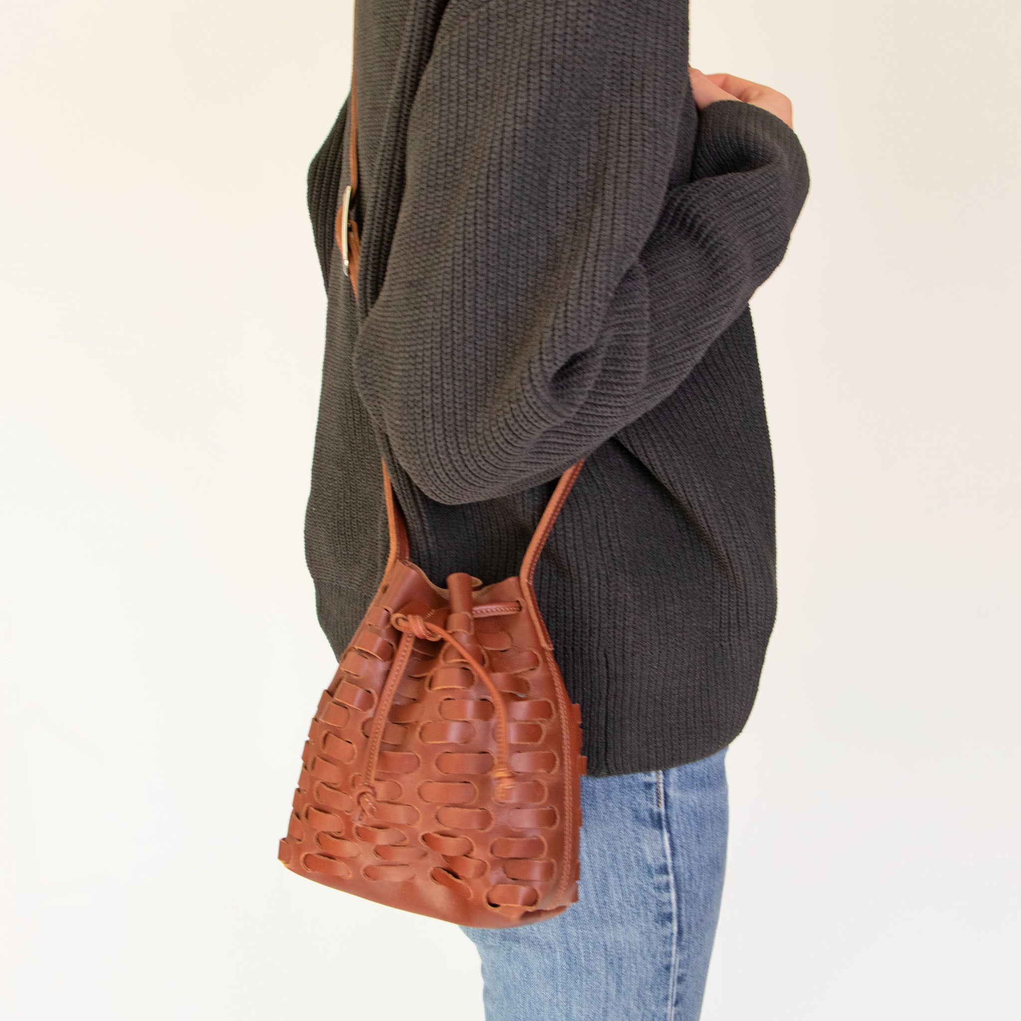 Person wearing a dark gray sweater and NImes weave bucket bag on a plain background