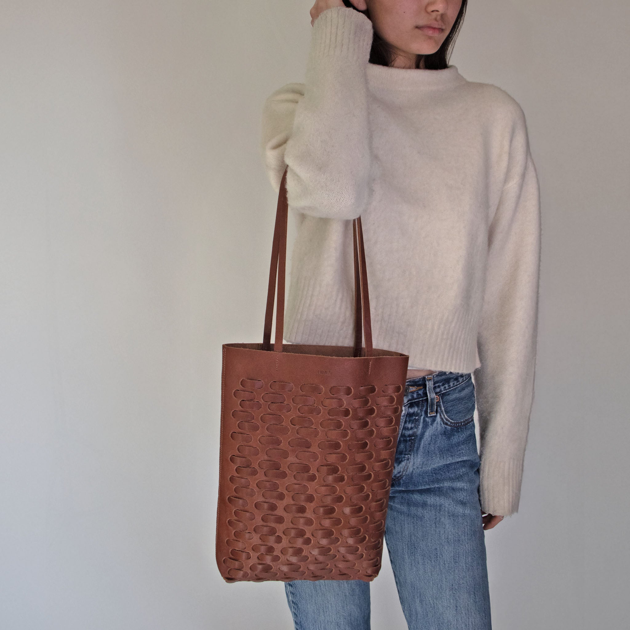 Person wearing a white sweater and NImes weave tote bag in tobacco on a plain background