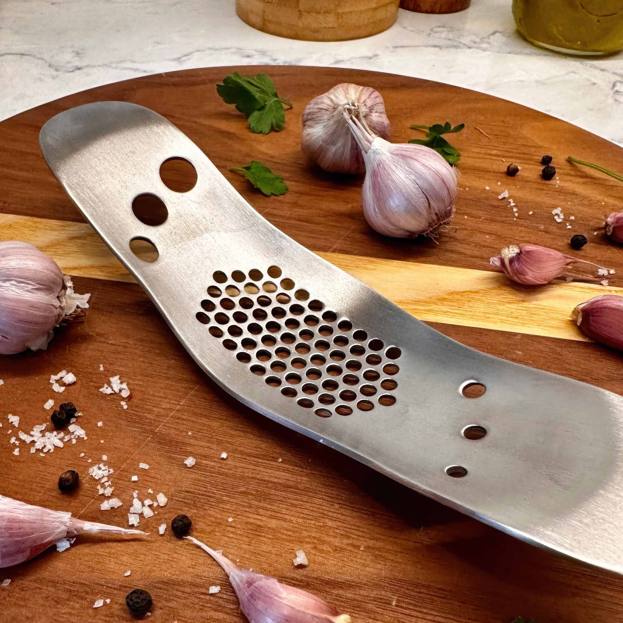 Metal herb stripper / garlic peeler on a wooden cutting board with garlic cloves and herbs