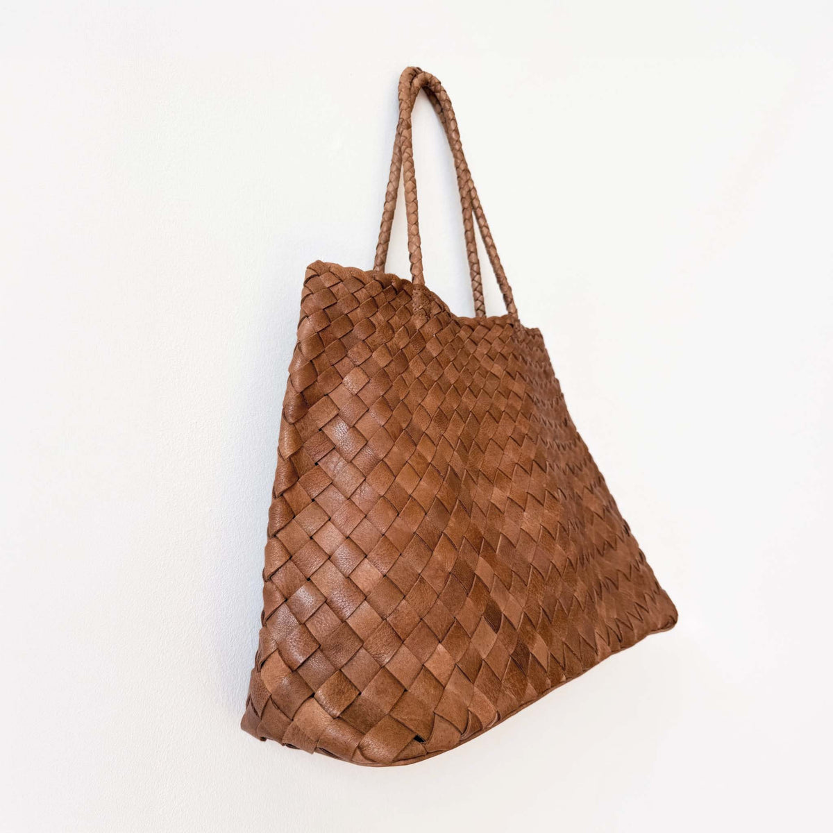 A brown woven leather tote bag with two shoulder straps, displayed against a plain white background.