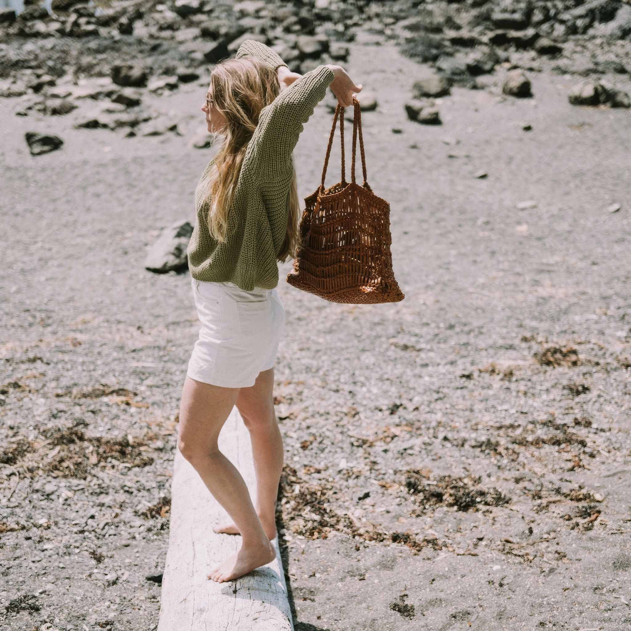Woman holding a woven leather bag on a rocky beach