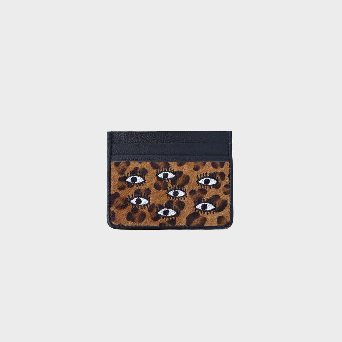 A small card holder with a black top section and a brown leopard print lower section featuring embroidered eyes, shown on a light gray background.