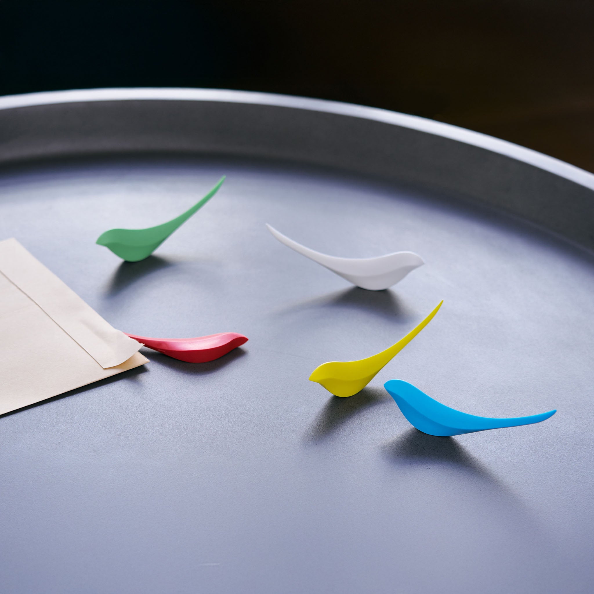 Colorful bird-shaped letter openers on a grey surface.