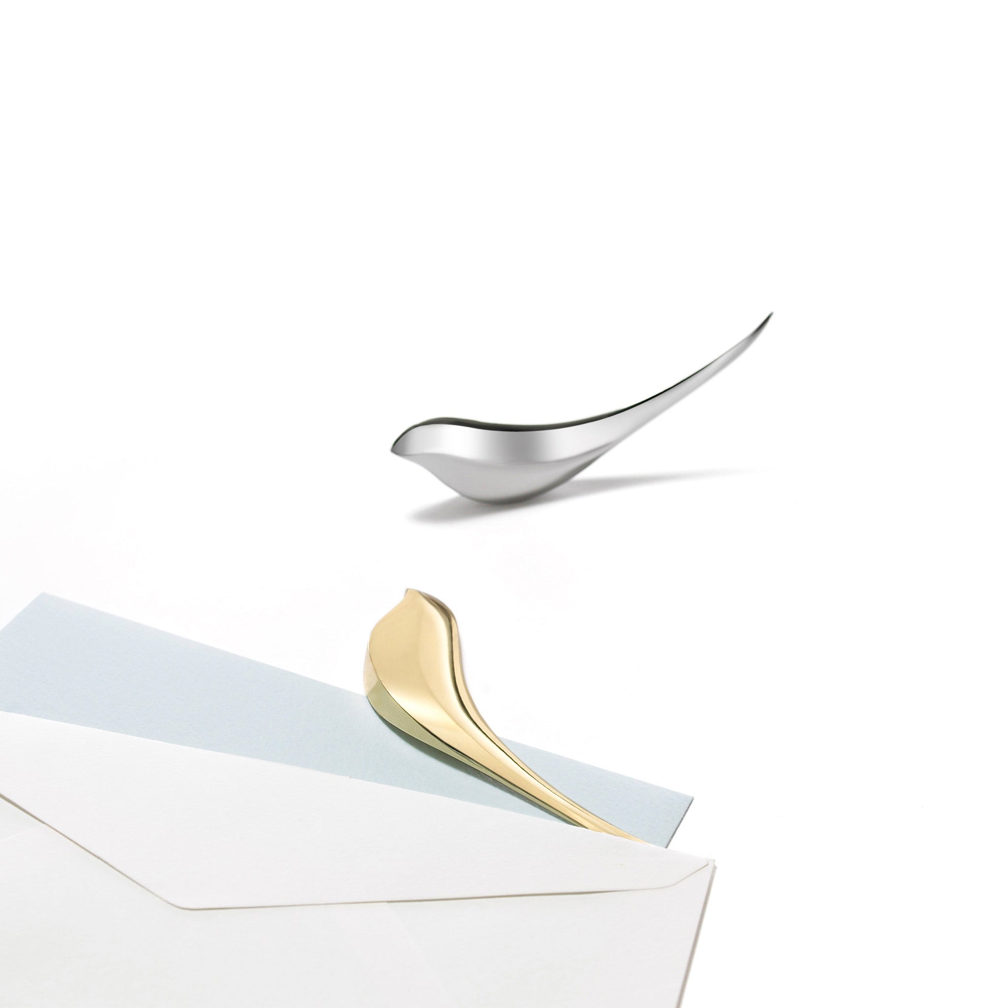 Gold and silver letter openers rest on a white surface with a white background