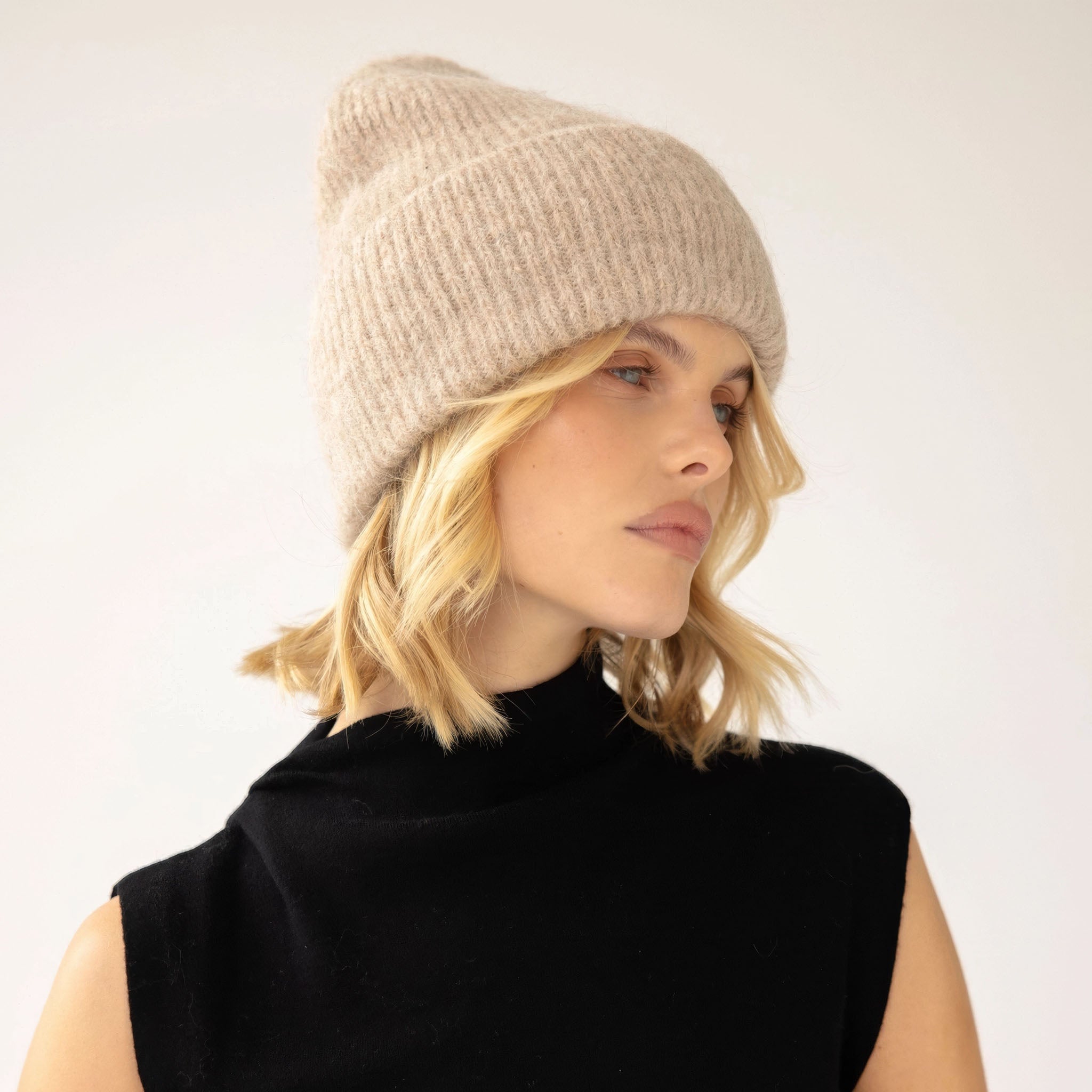 Model wearing an iced taupe knit beanie and black sleeveless top on a white background