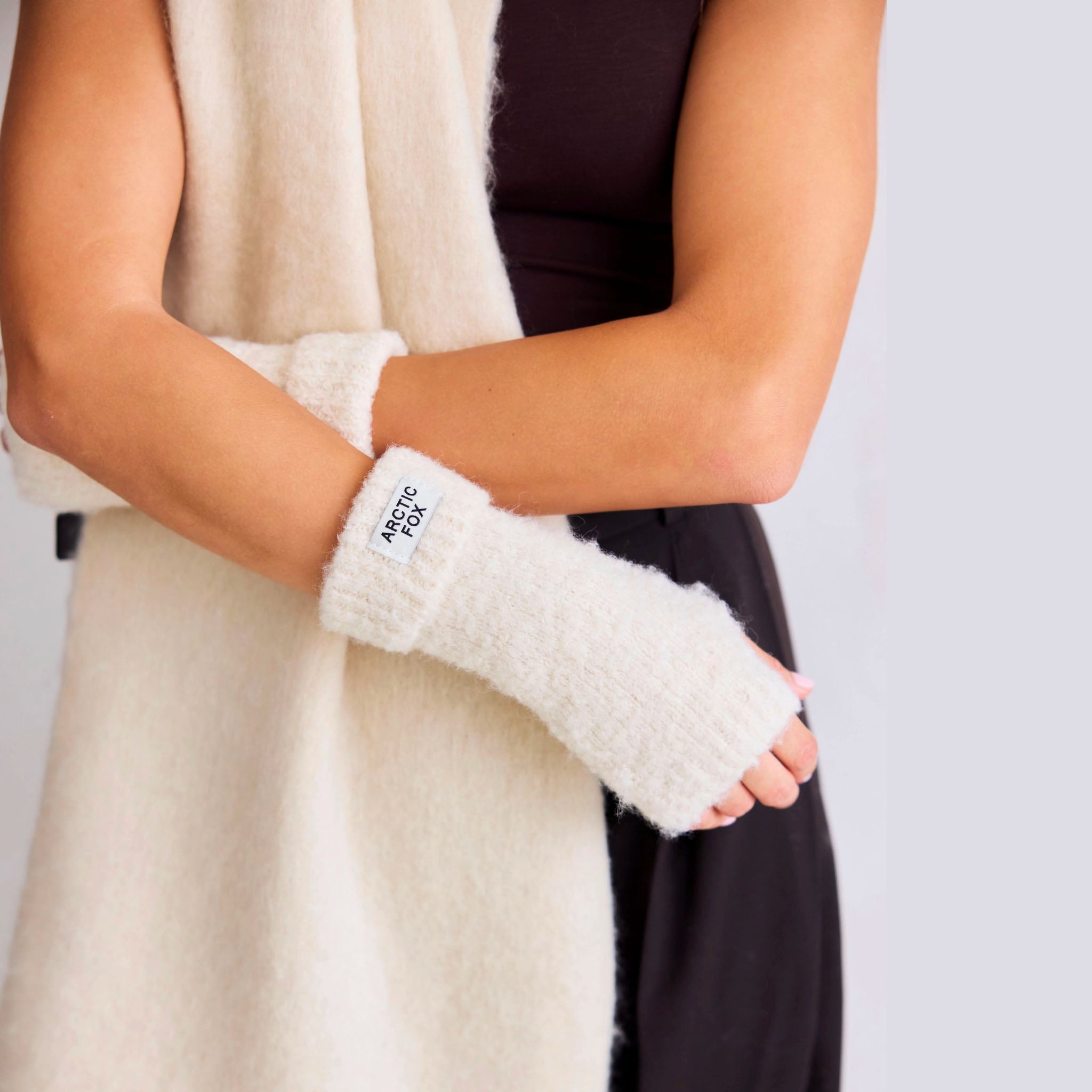 Person wearing pebble beige fuzzy hand warmers with a visible brand label on a neutral background