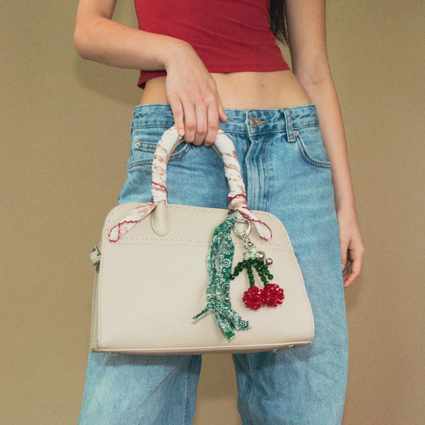 Model holding a beige handbag with decorative elements against a beige background