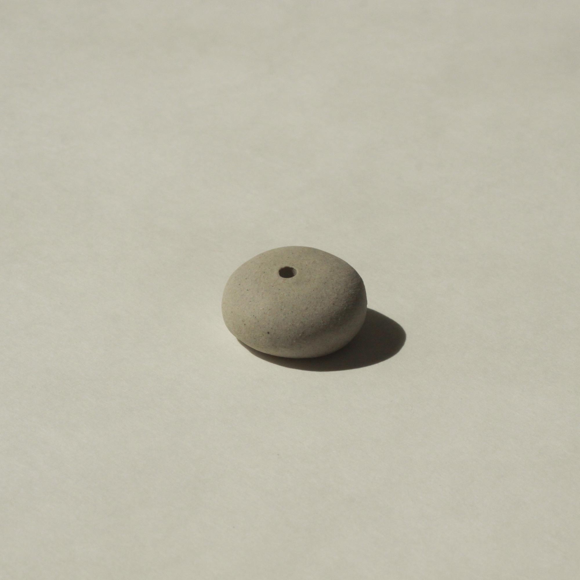The underside of a mini light grey ceramic pebble incense holder