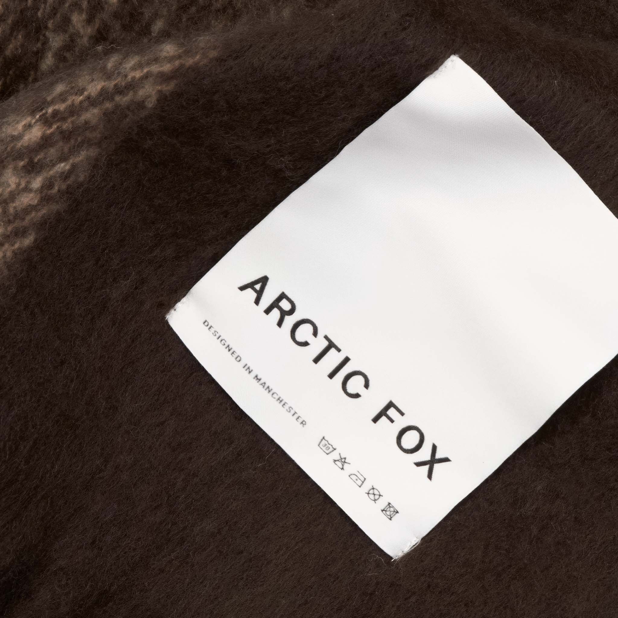 Close-up of the plaid throw with brown, beige, and white pattern and label 'Arctic Fox'
