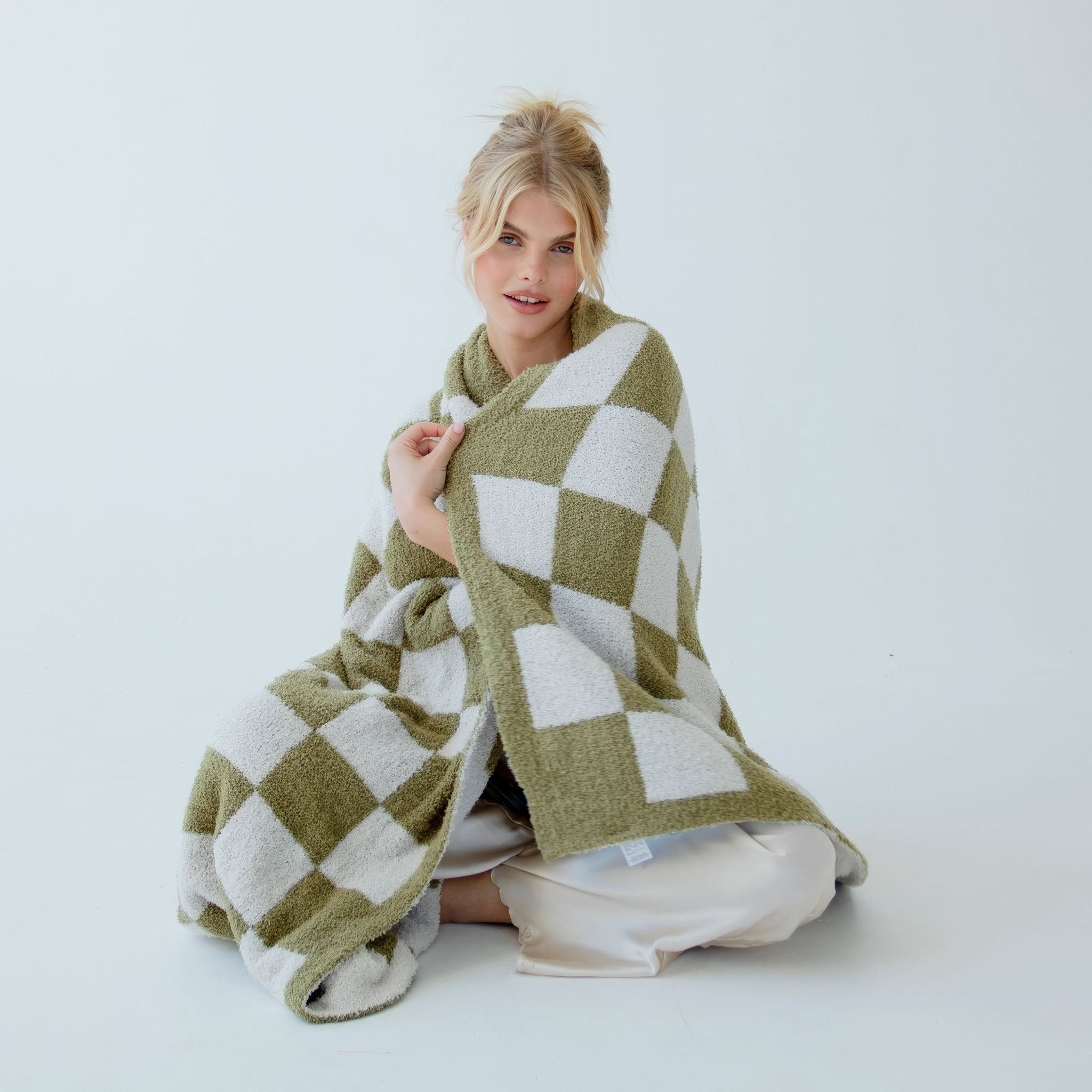 Model wrapped in a moss green and white checkered blanket on a light background