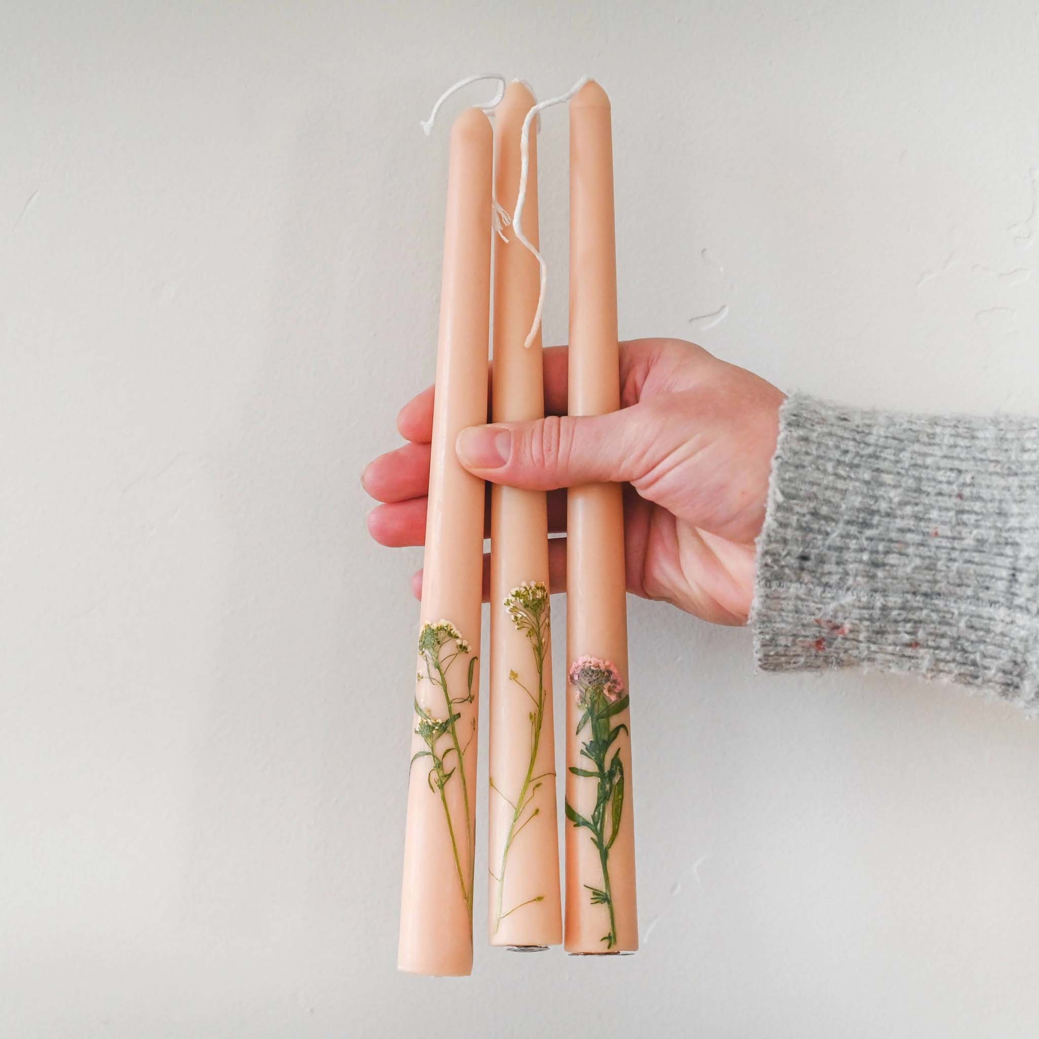Someone holding three nude floral inlaid tapered candles