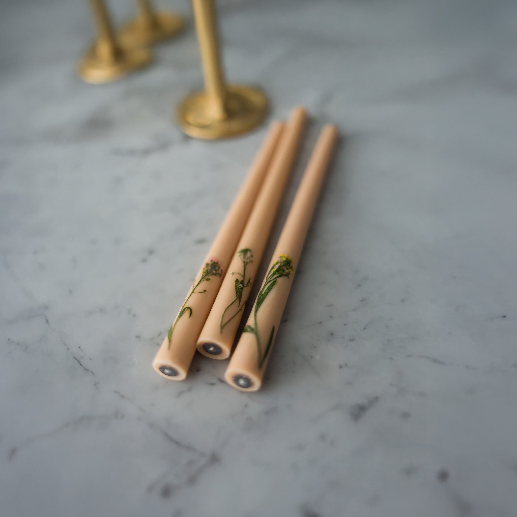 Image of three nude floral inlaid tapered candles on a marble top