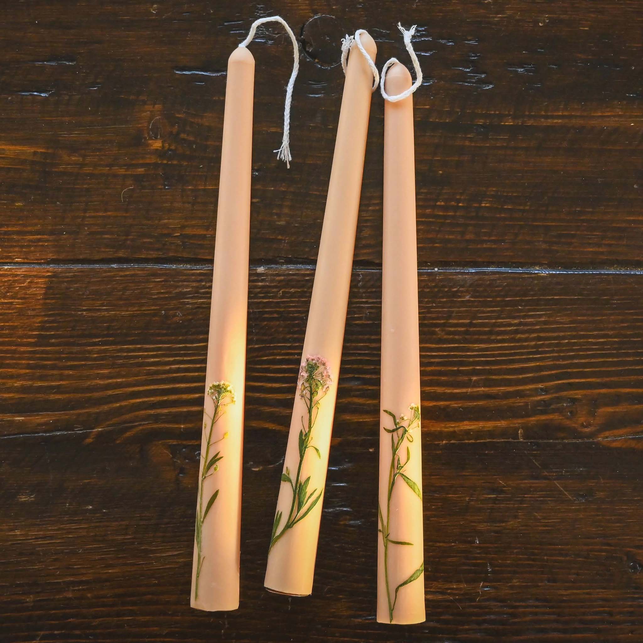 Image of three nude floral inlaid tapered candles on a wooden table