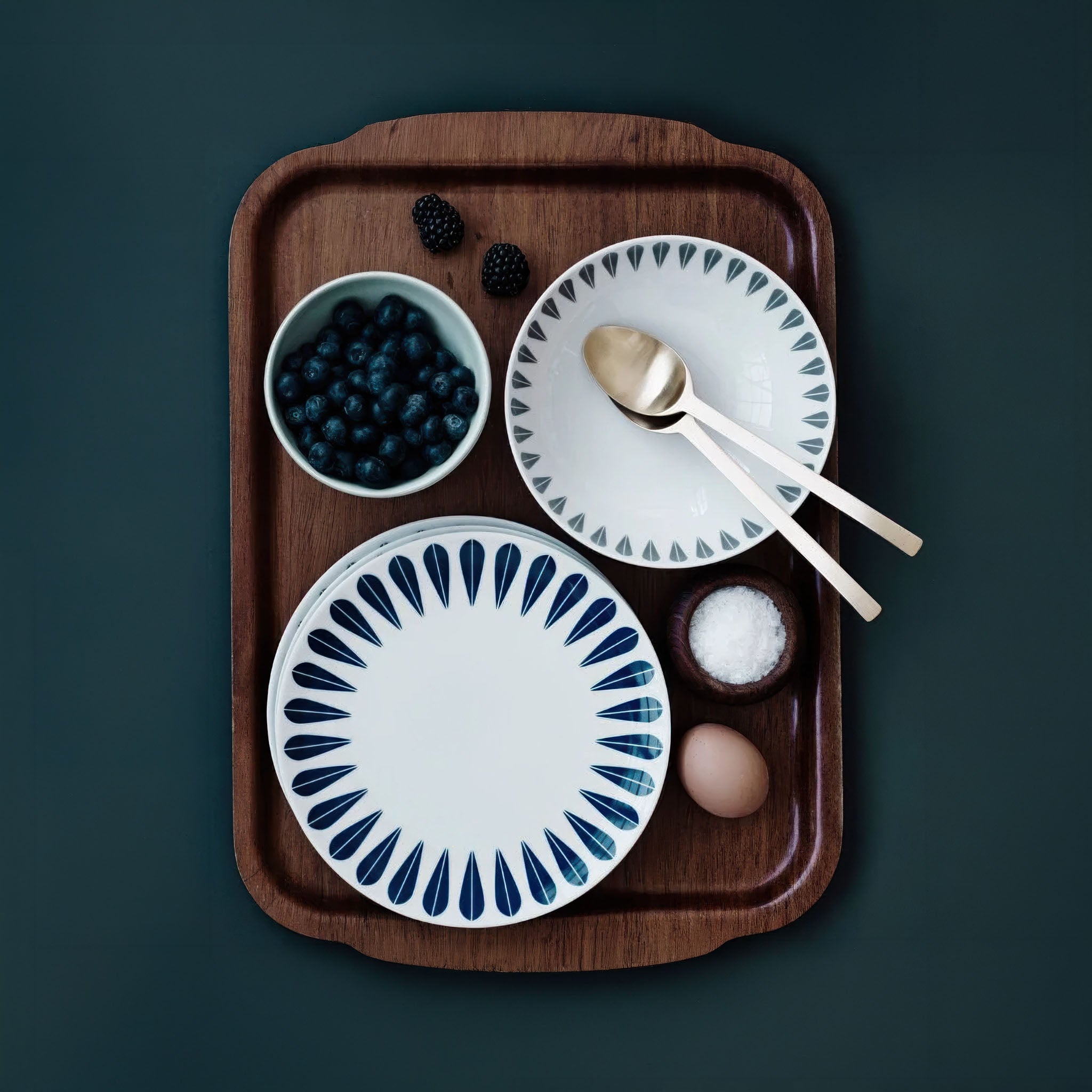 Wooden tray with ceramic lotus plates, bowls, and utensils on a dark background