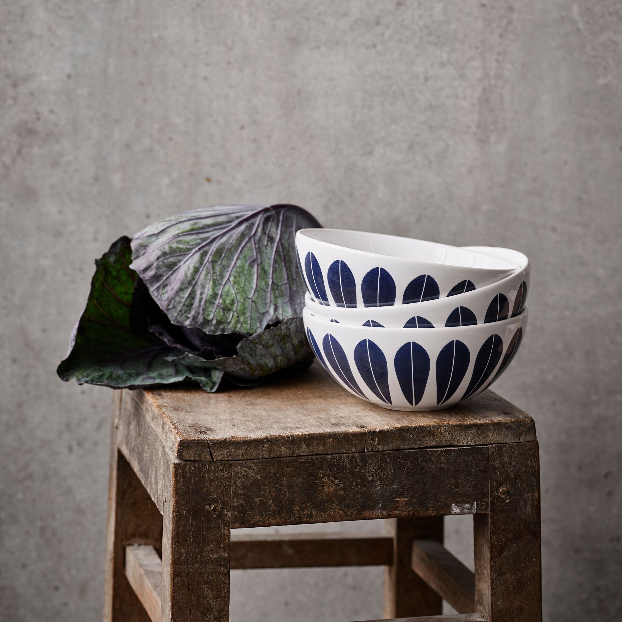 Image of Lucie Kaas's Arne Clausen decorative white/blue bowls stacked next to a bunch of vegetables on a vintage wooden stool