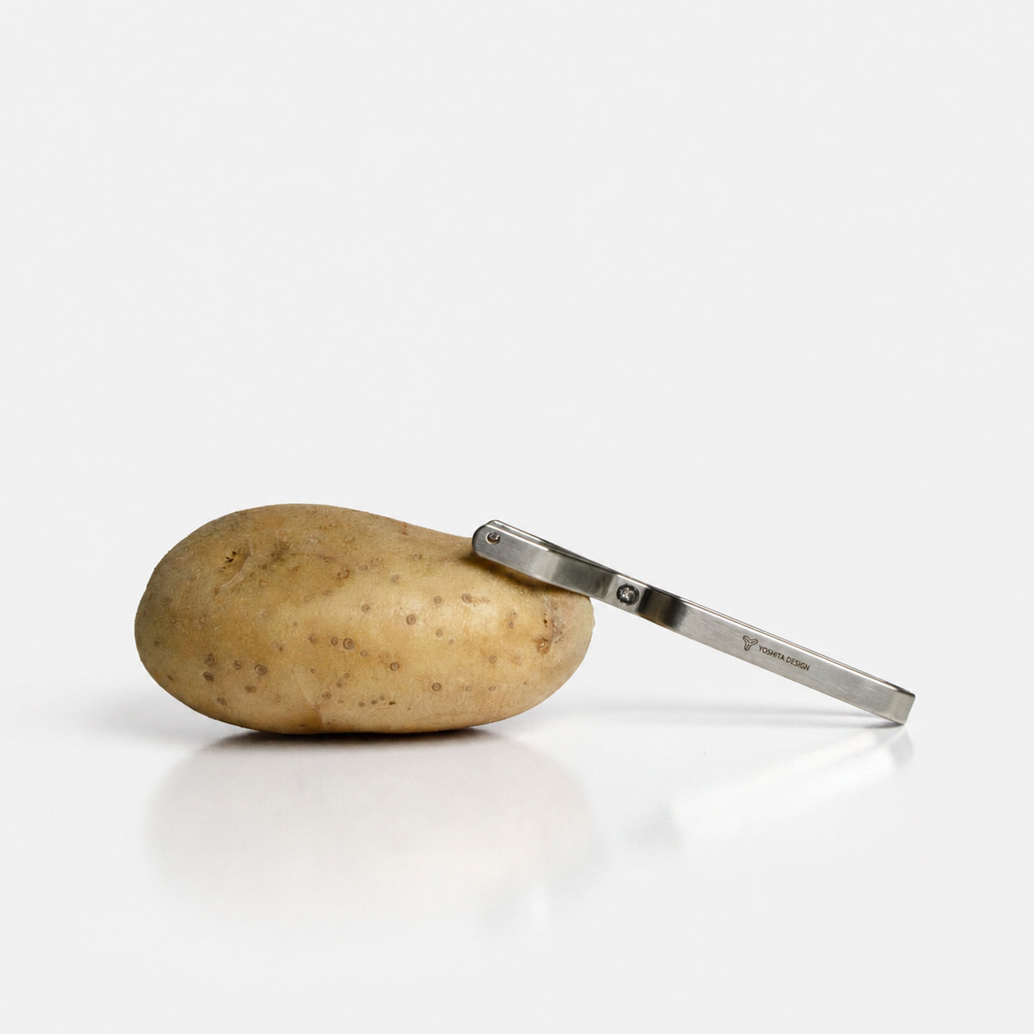 A potato and the Yoshital stainless steel peeler on a gray background