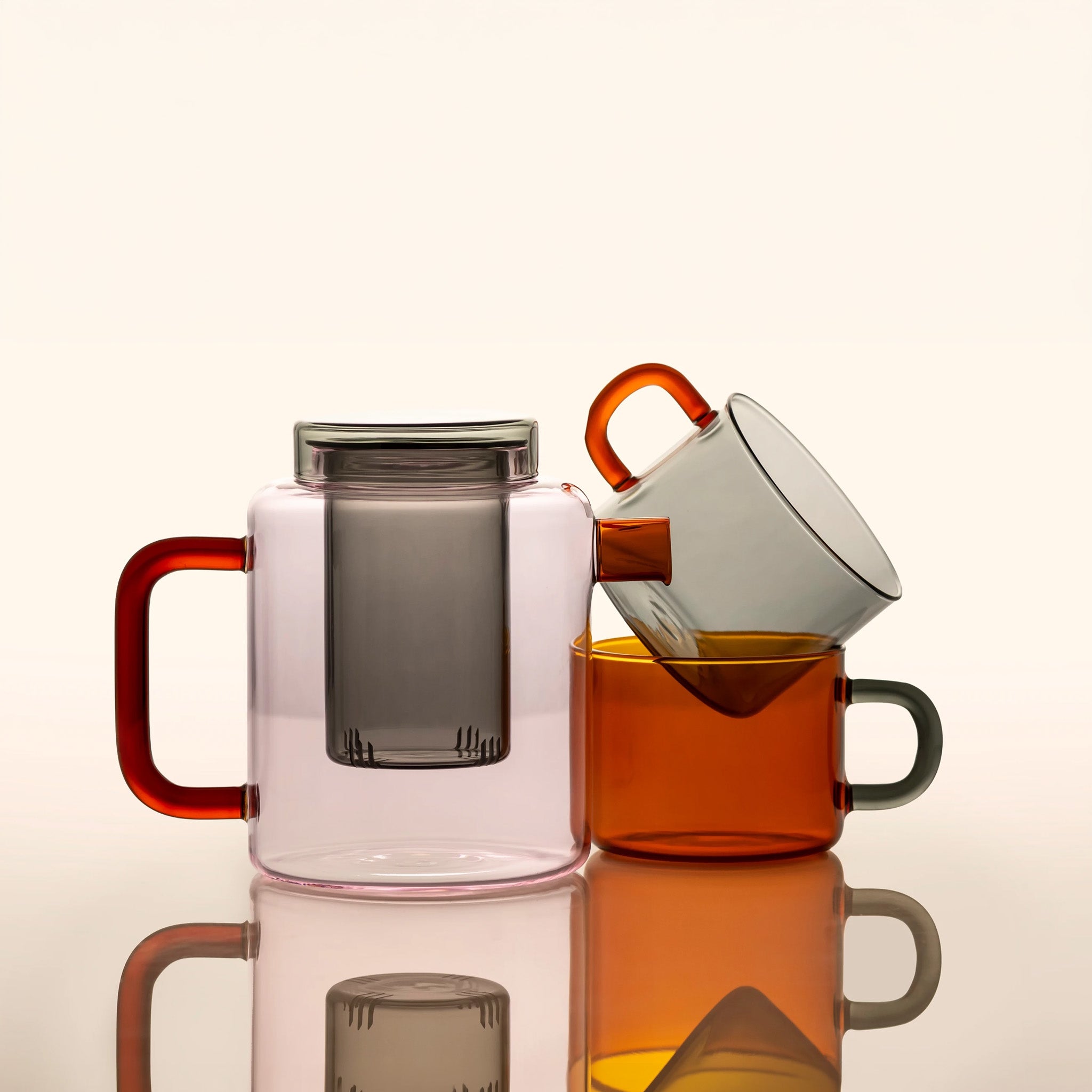 A Pink Flamingo Cha Pot with a mug set of the Eye of the Tiger colorway arranged on a reflective surface against a warm off-white background.