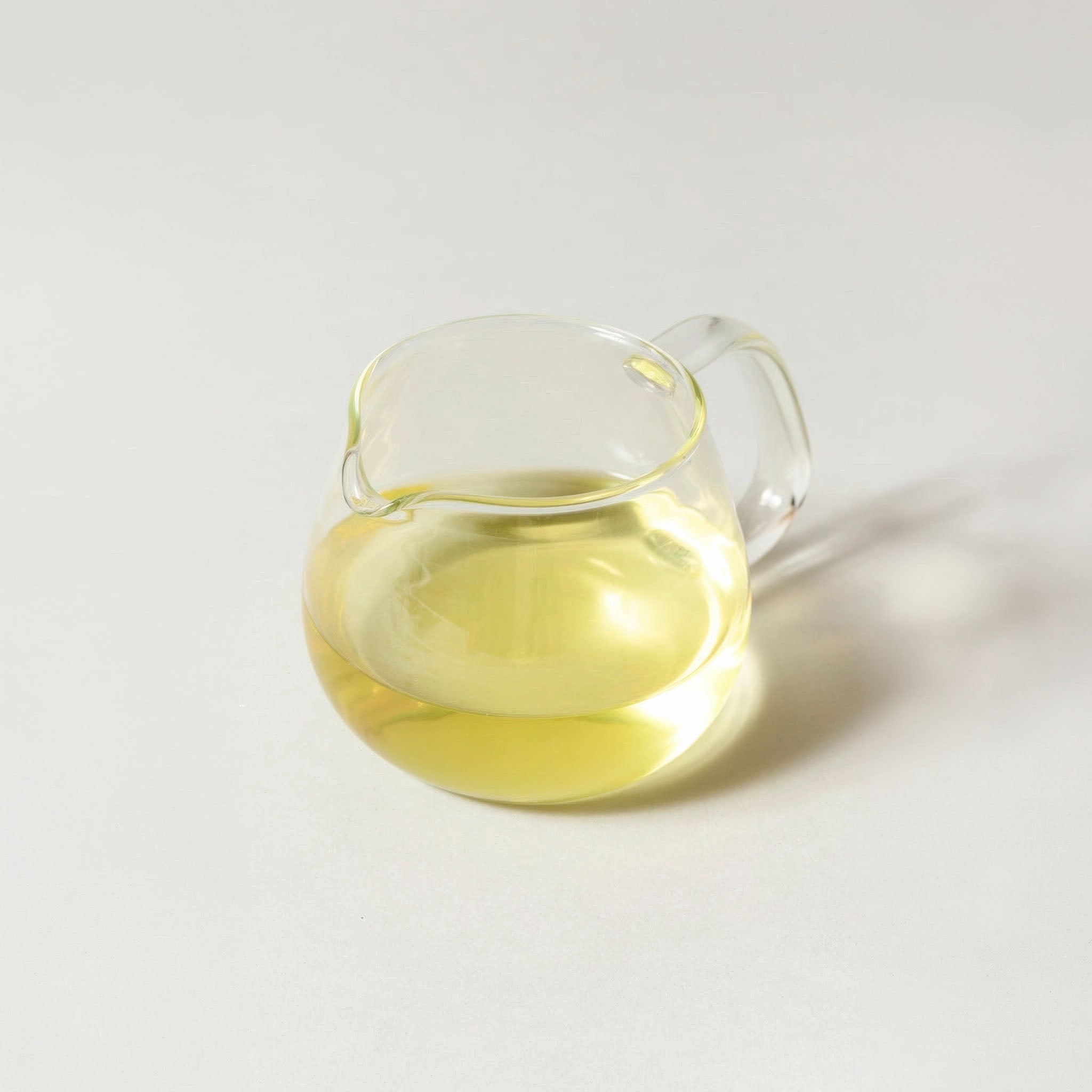 Clear glass tea cup with a handle filled with genmaicha on a white background