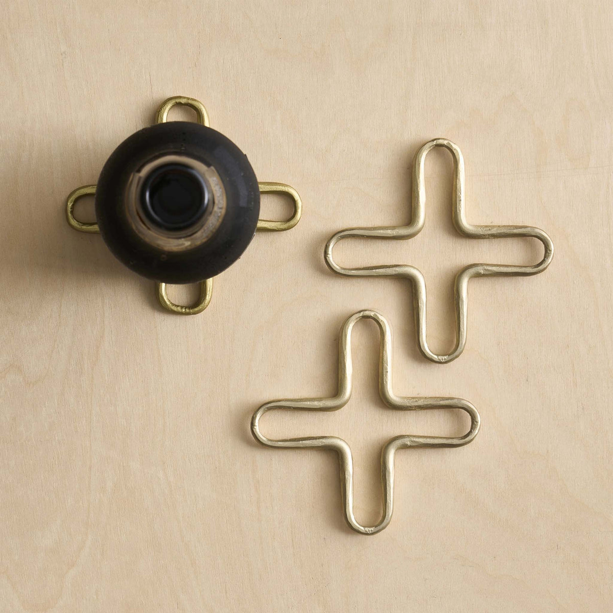 A trio set of brass mini trivets with a black pot on one side on a light wood background.