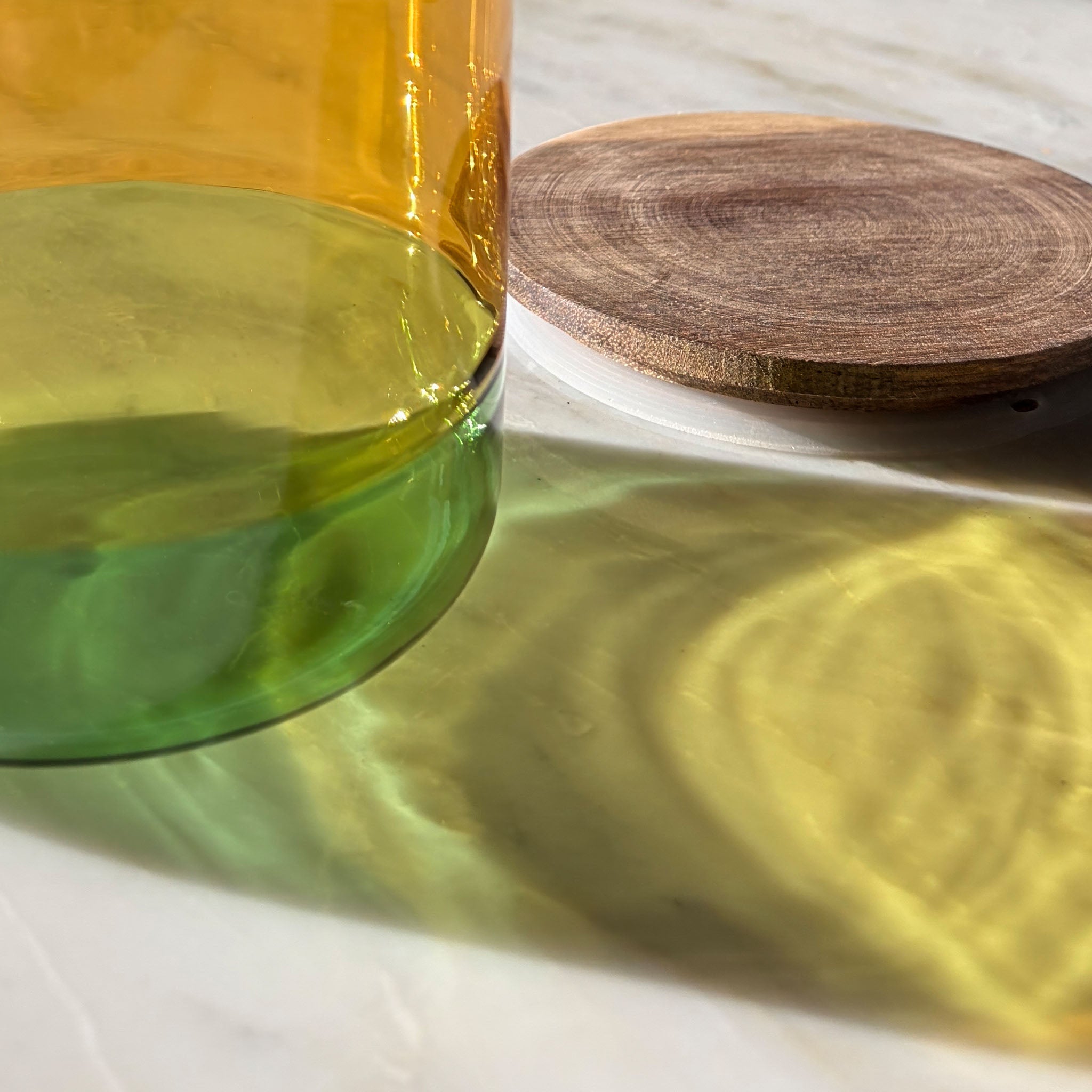 Close-up of yellow and green cylindrical glass canister with a wooden lid on a white background