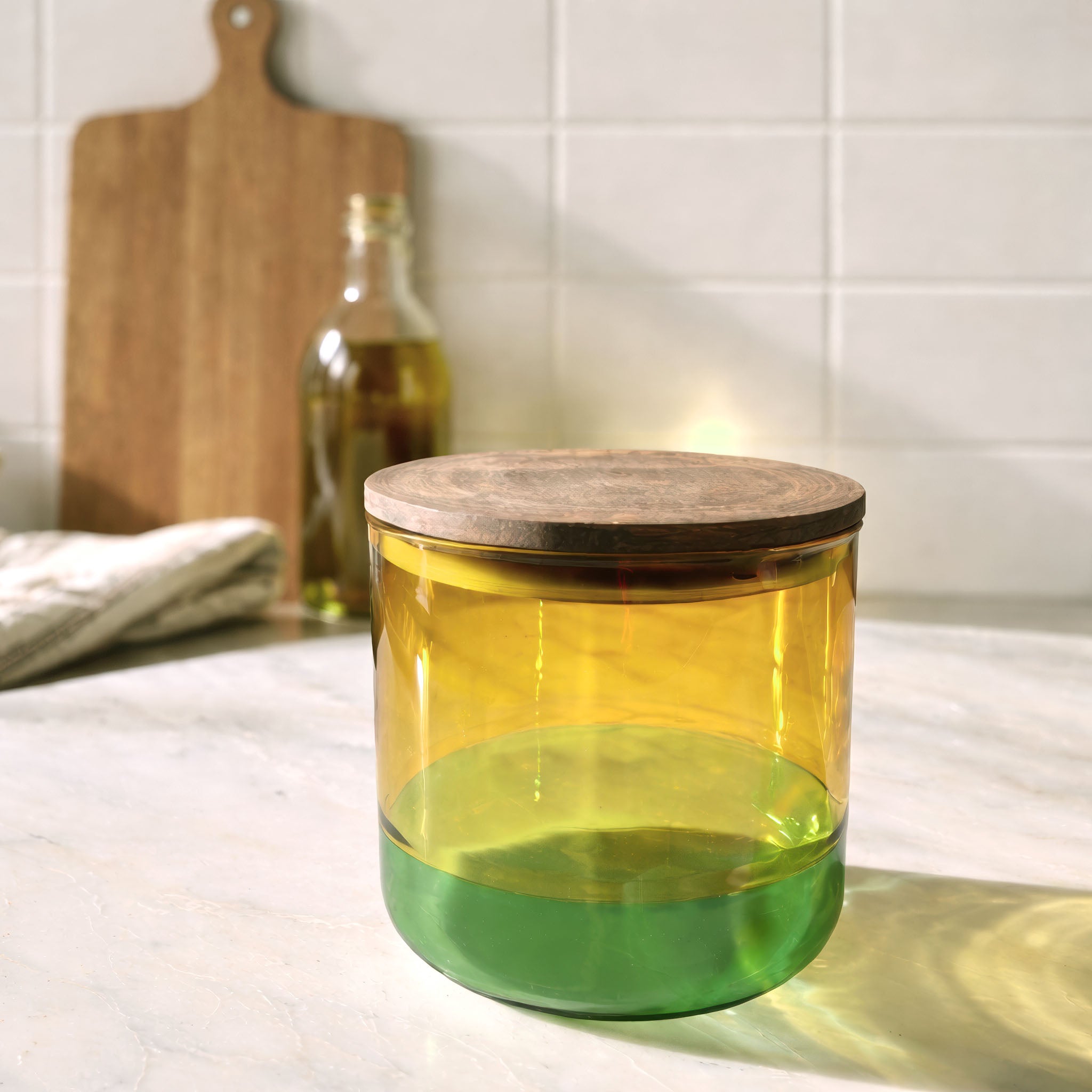 Yellow and green cylindrical glass canister container with wooden lid on a kitchen counter