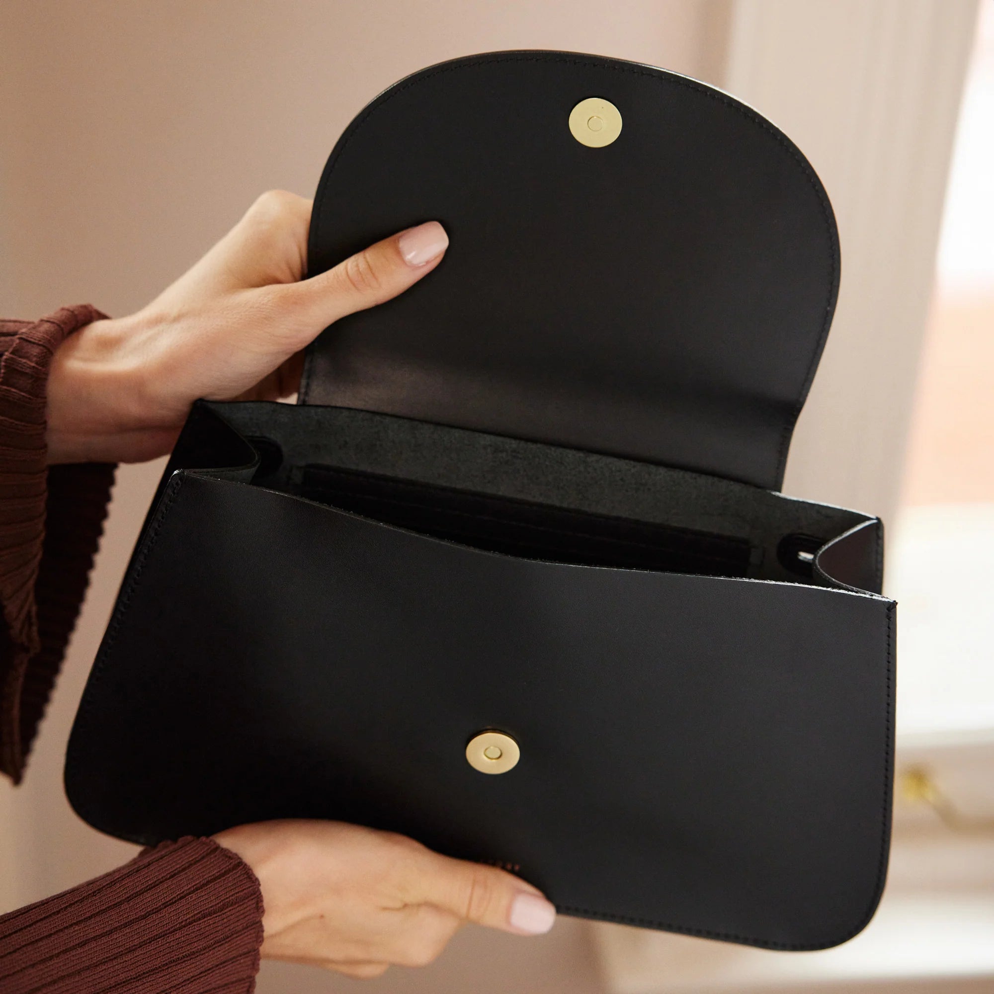 A hand model holding open Minor History's The Horizon Crossbody bag in black