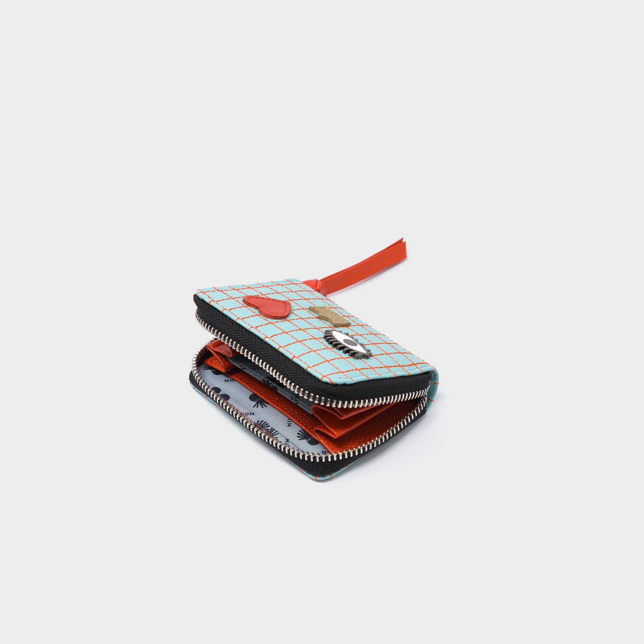 Multicolored zippered wallet with a grid pattern, eye, heart, and crown designs on a light gray background