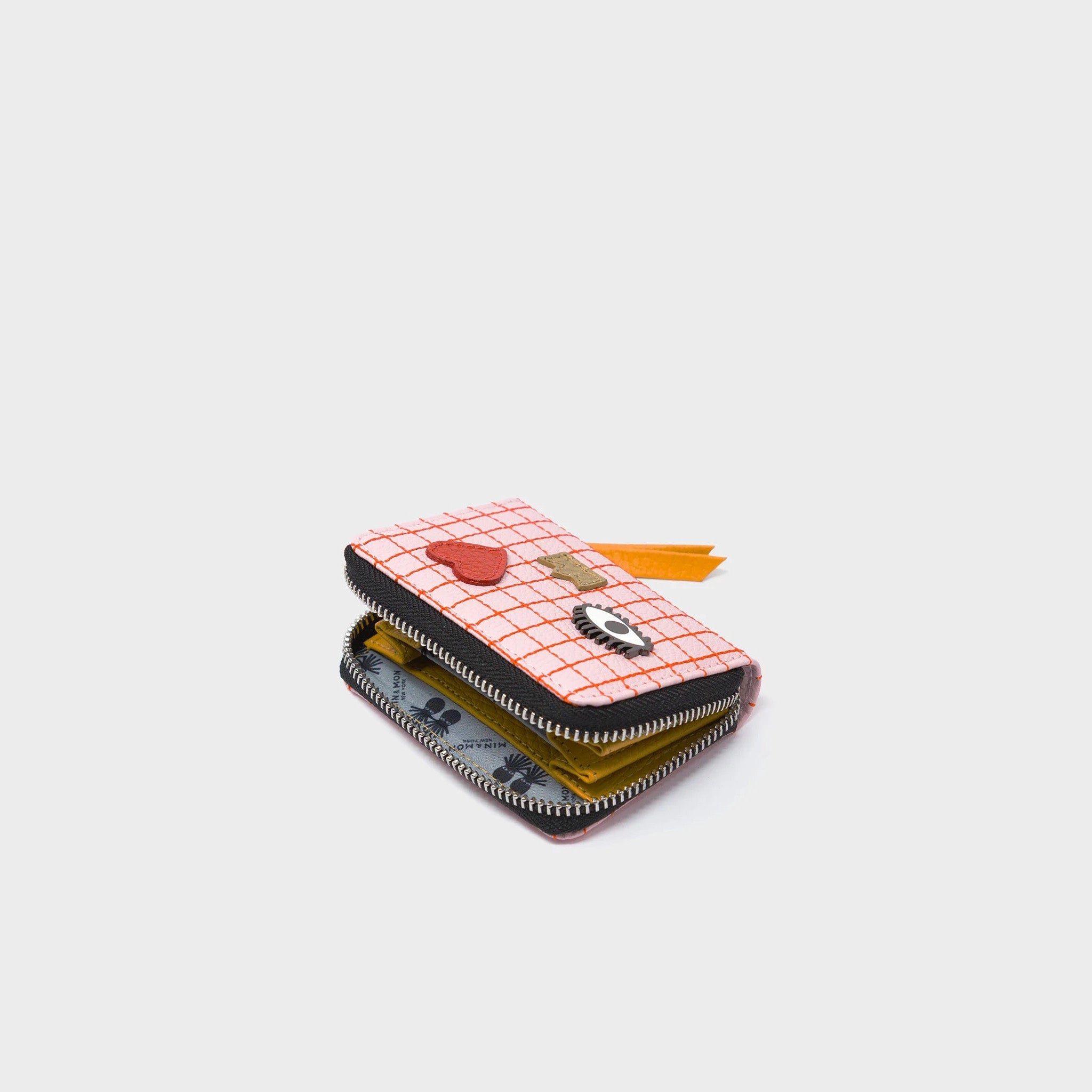 Small wallet with a pink checkered pattern, eye design, and red heart opened and laid on a white background