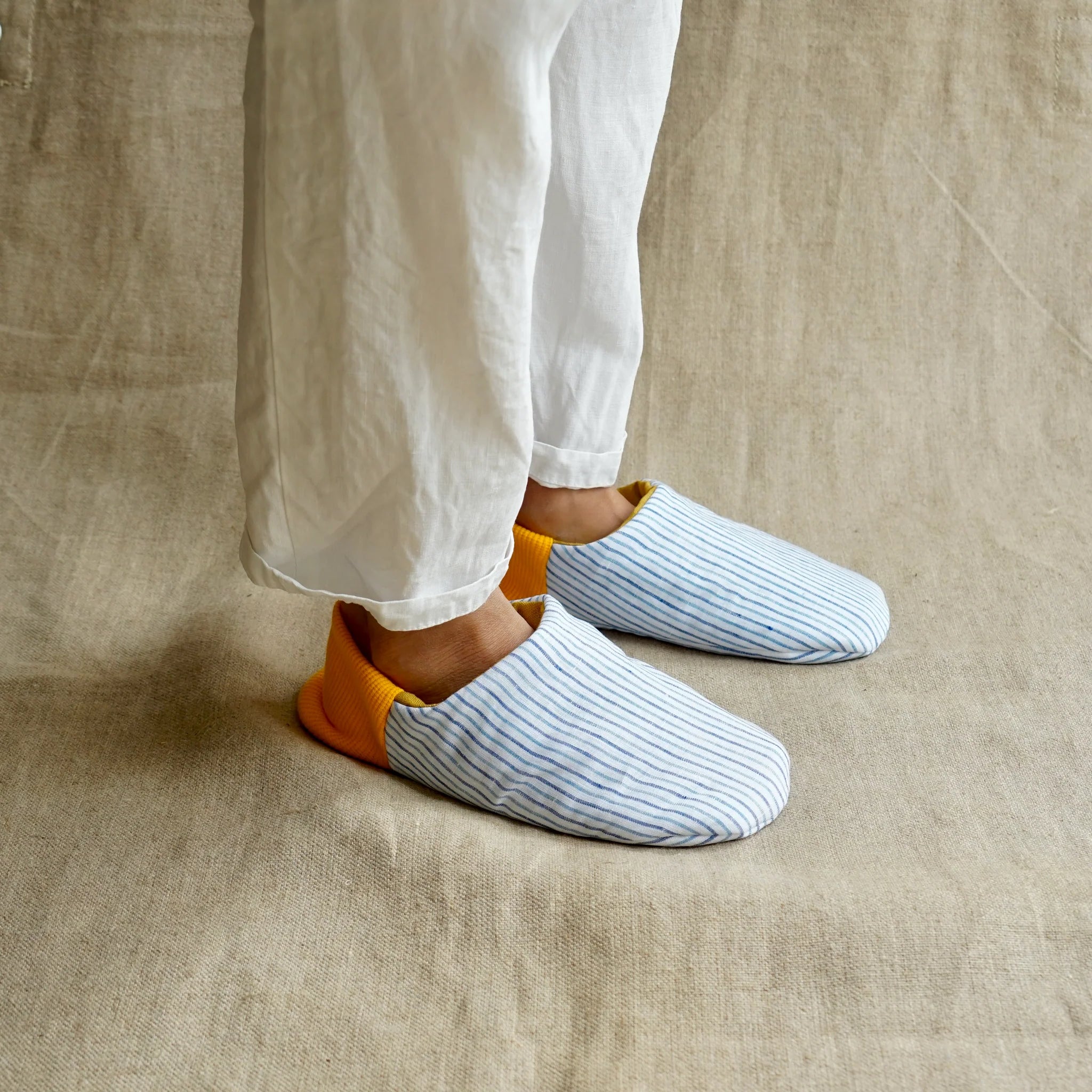 Person wearing white striped slippers with yellow accents on a beige fabric background