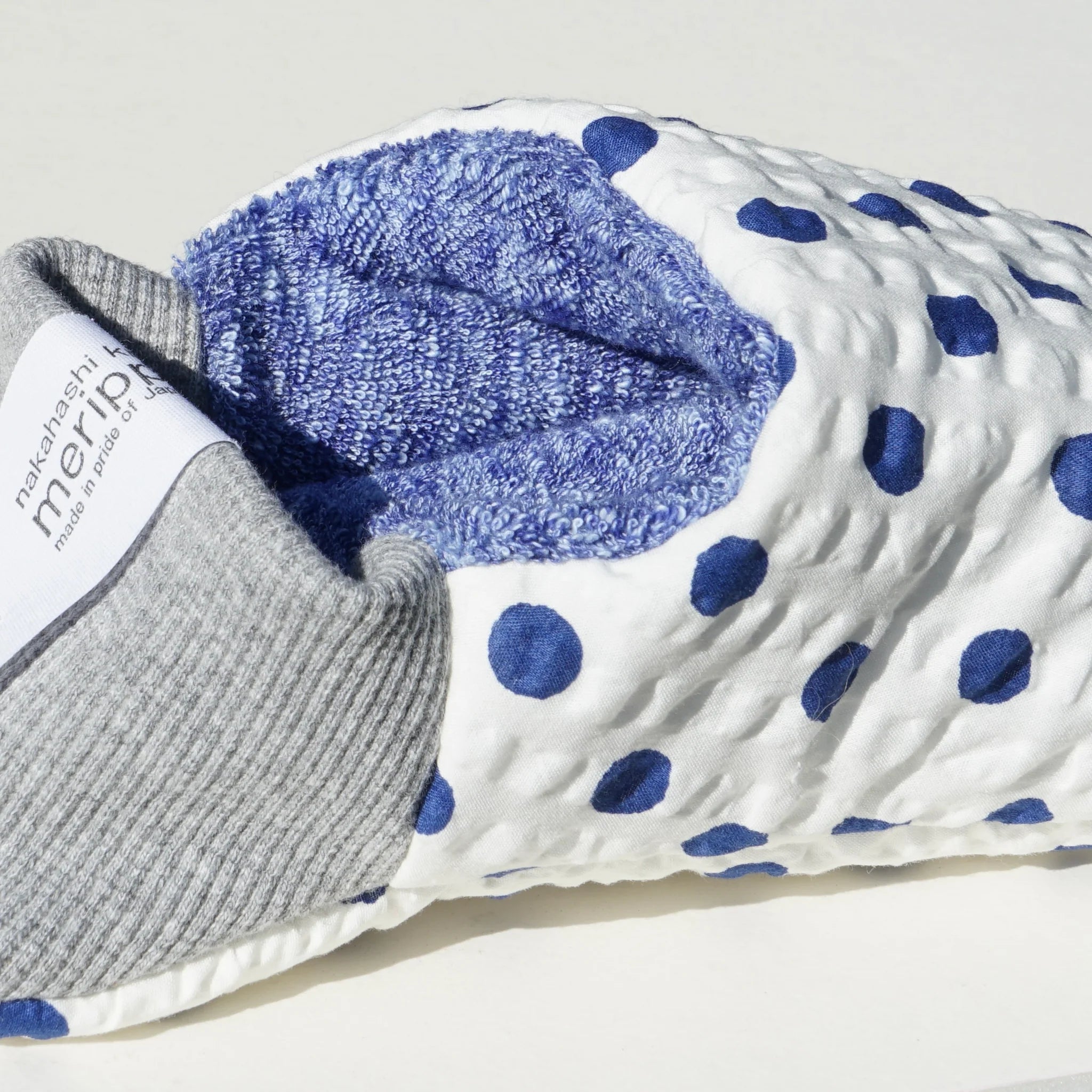 Close up of blue and white polka dot slippers with blue interior and gray heels on a white background