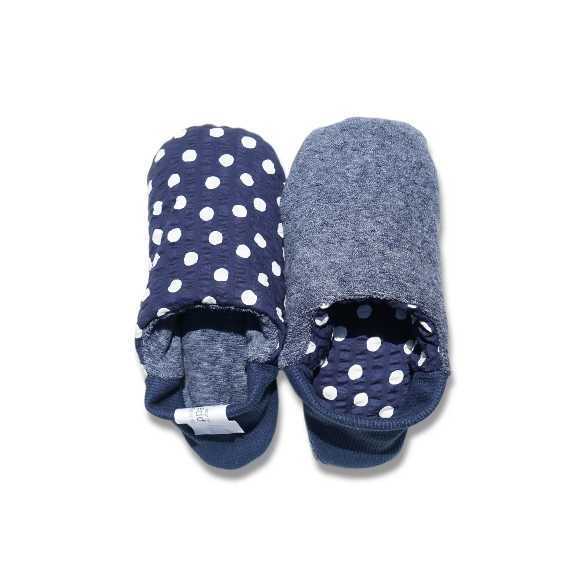 Pair of navy blue and white polka dot slippers with blue interior and blue heels on a white background