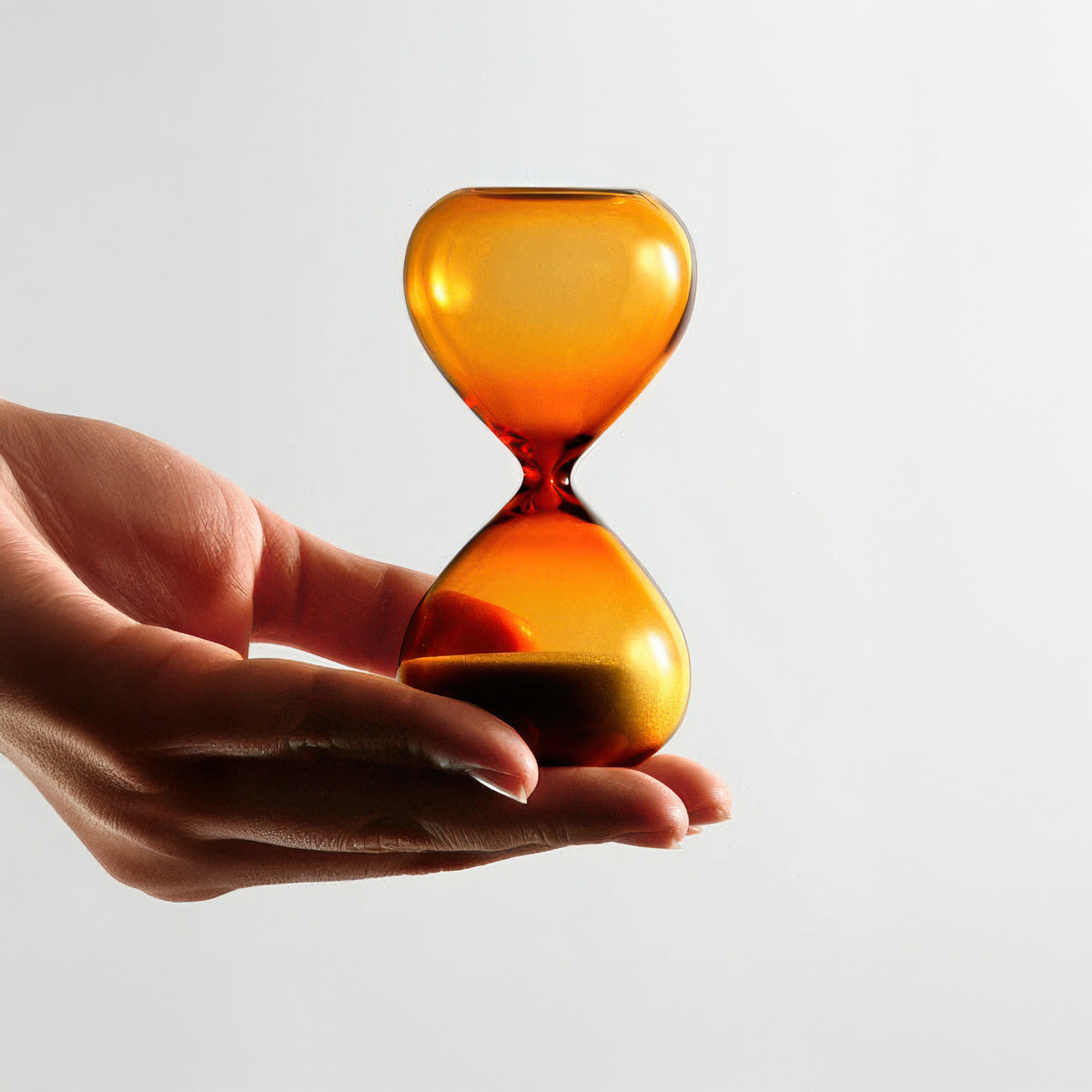 Hand holding a small amber hourglass against a light gray background