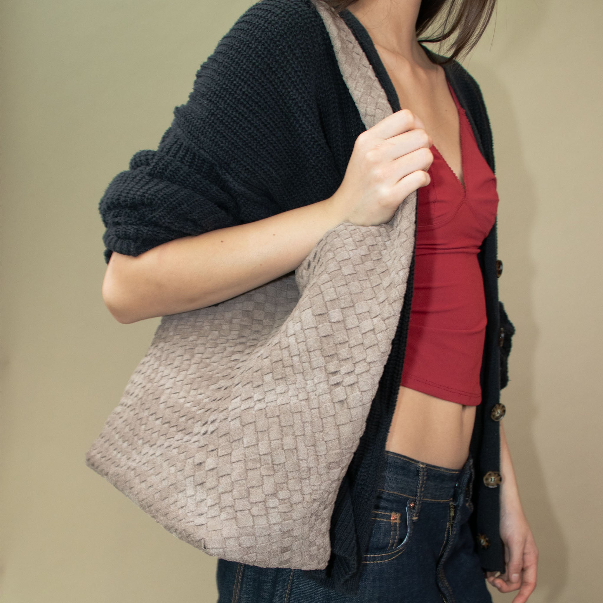 Model wearing a dark blue cardigan over a red top with a woven vegan suede clay colored bag.