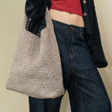 Model wearing a dark blue cardigan over a red top with a woven vegan suede clay colored bag.