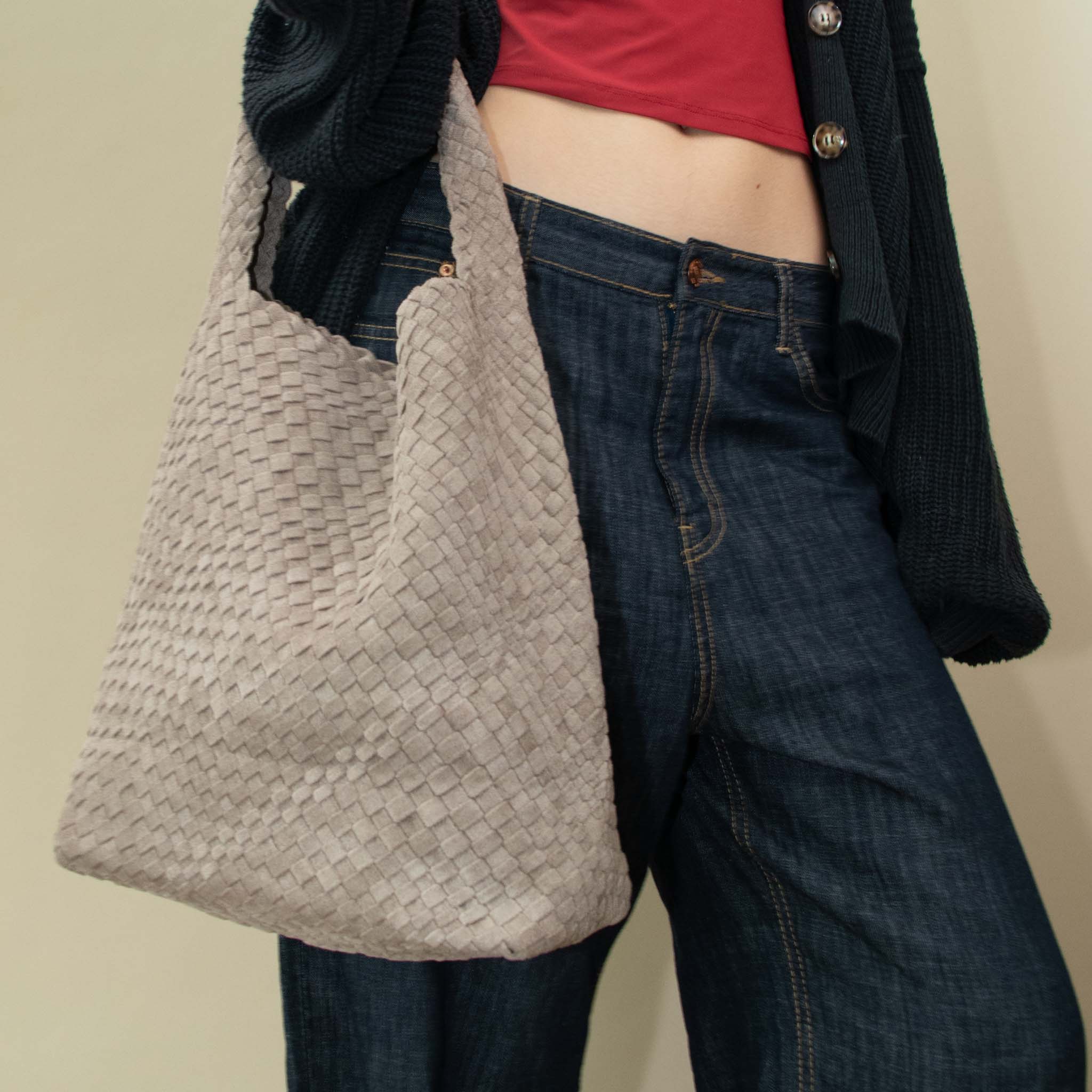 Model wearing a dark blue cardigan over a red top with a woven vegan suede clay colored bag.
