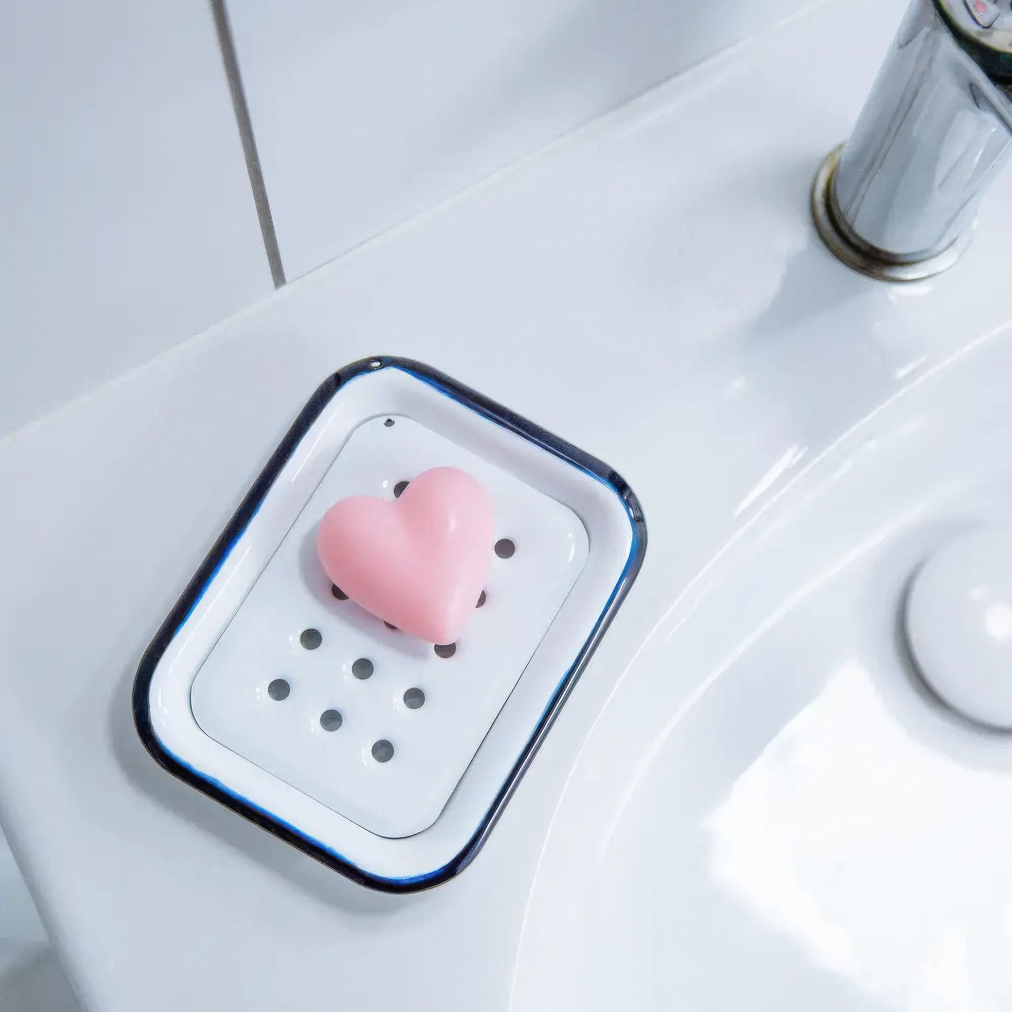 Heart-shaped pink soap on a white soap dish in a bathroom sink.
