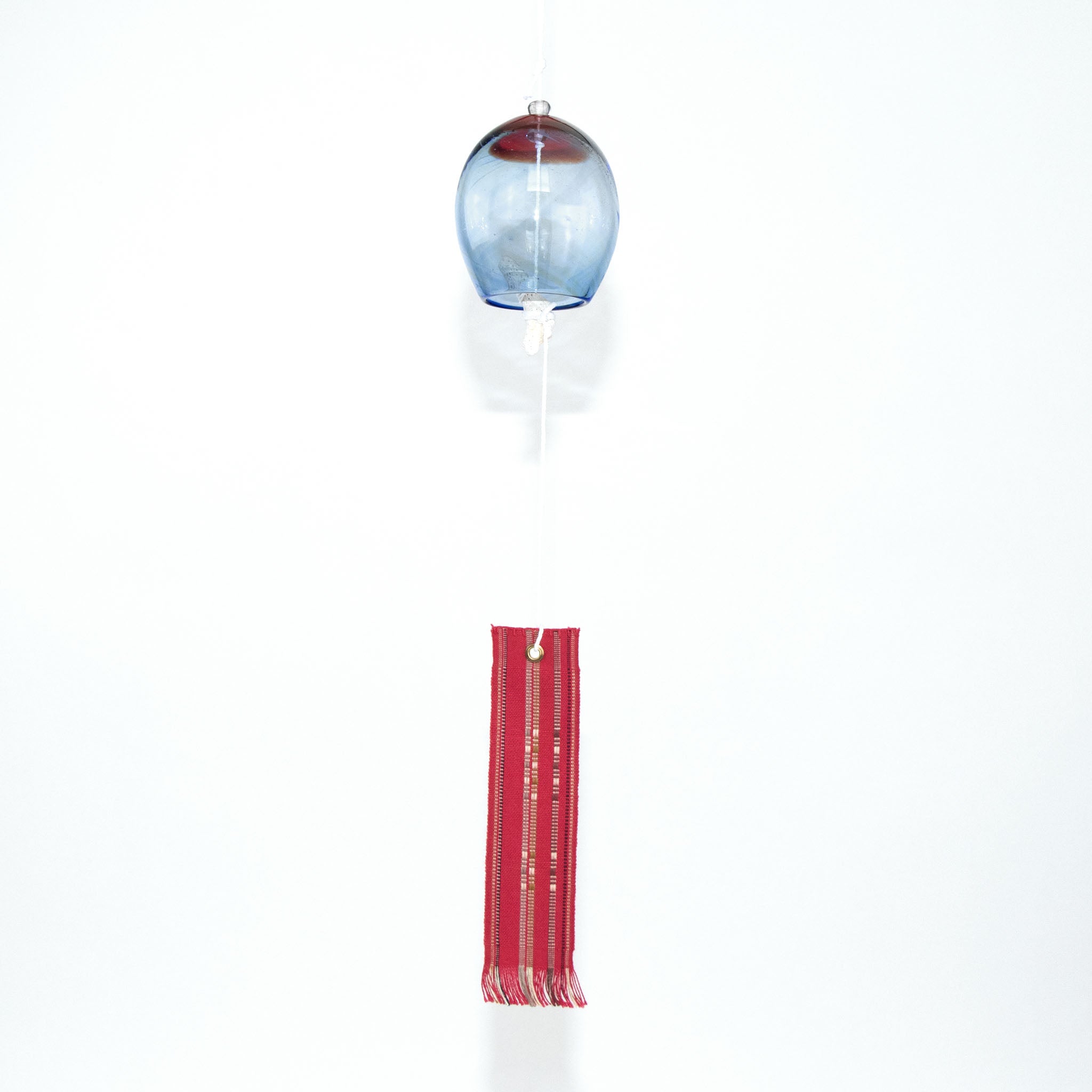 Blue and red glass Okinawan wind chime with red handwoven tab by Miyahira Studio, suspended on a white background.
