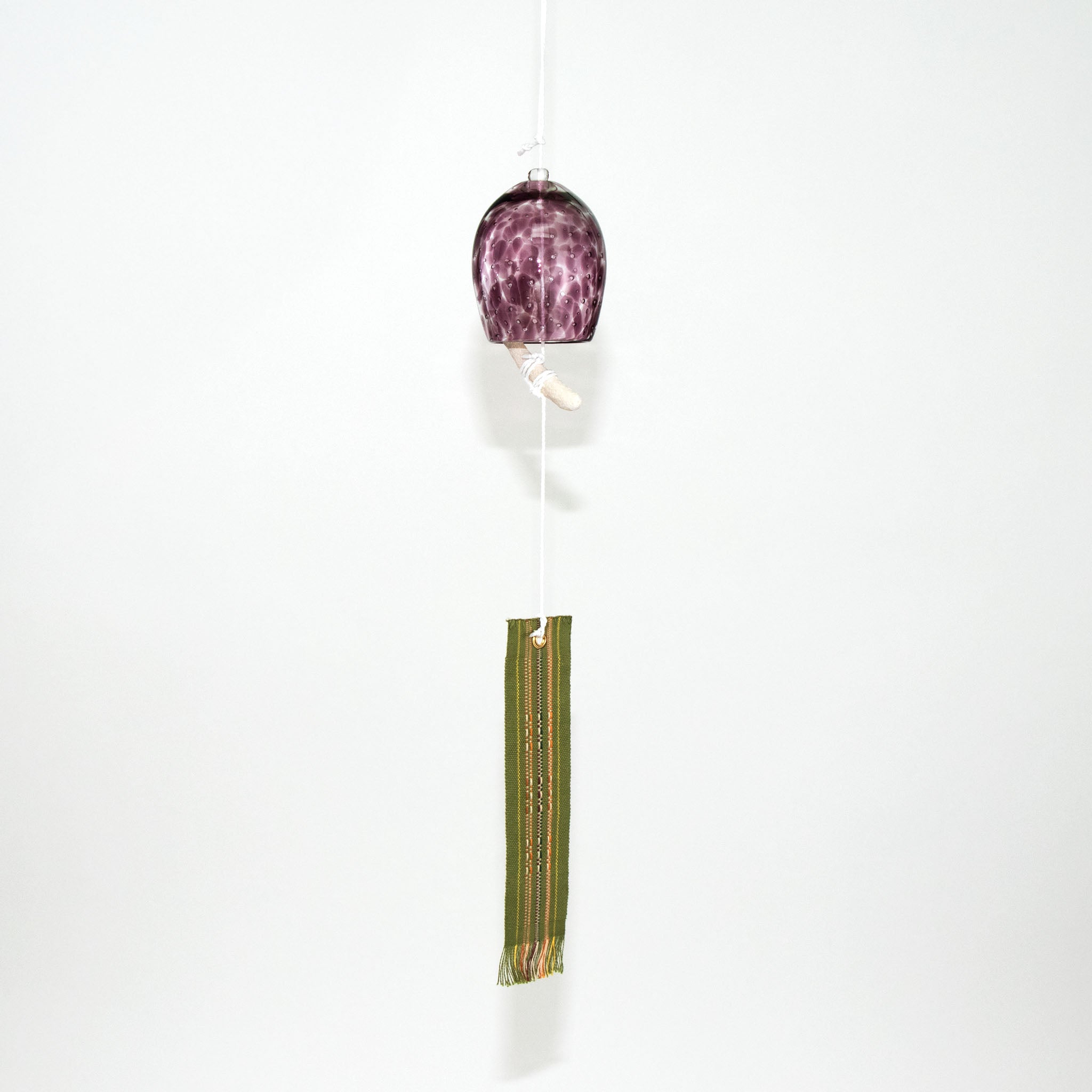 Rose pink glass Okinawan wind chime with green handwoven tab by Miyahira Studio, suspended on a white background.