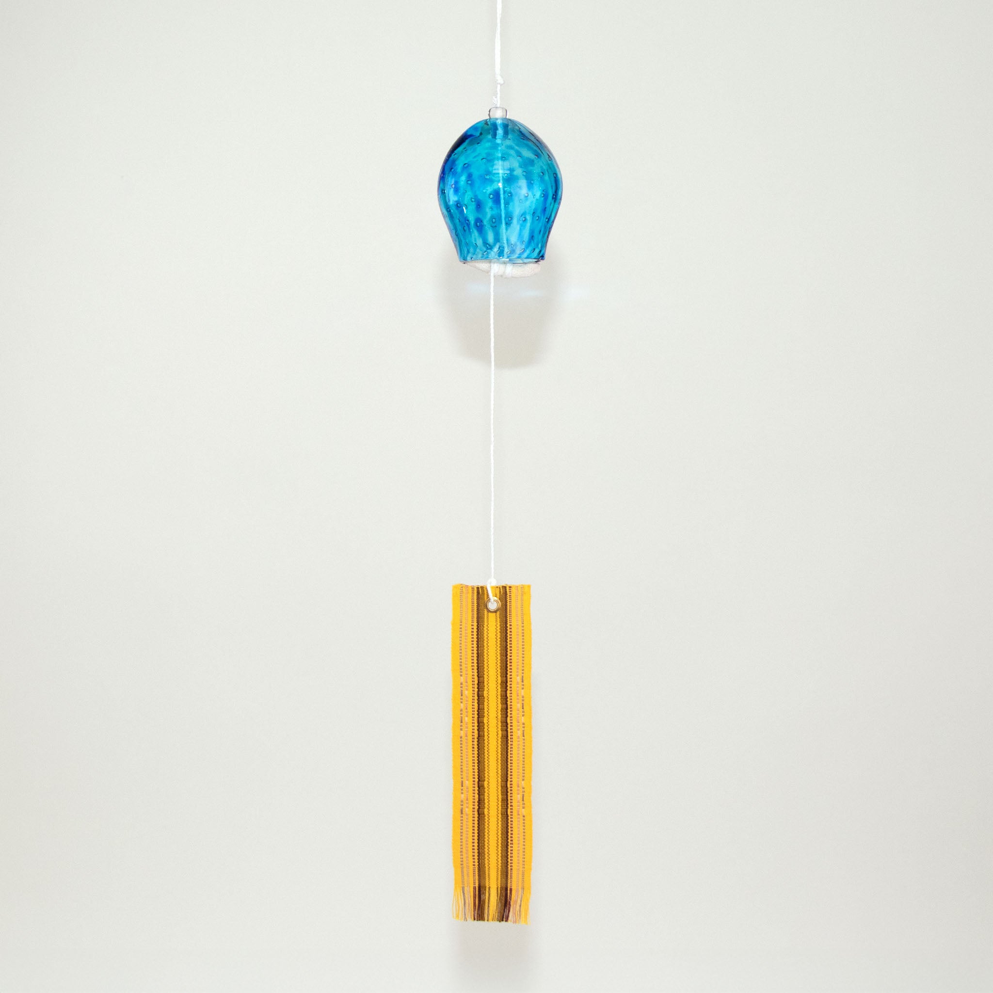  Blue glass Okinawan wind chime with yellow handwoven tab by Miyahira Studio, suspended on a white background.