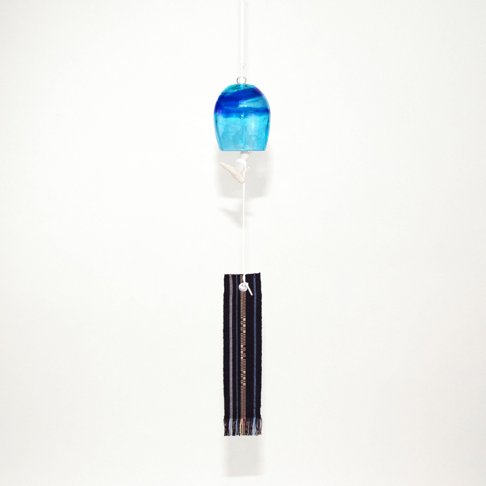 Blue glass Okinawan wind chime with black handwoven tab by Miyahira Studio, suspended on a white background.