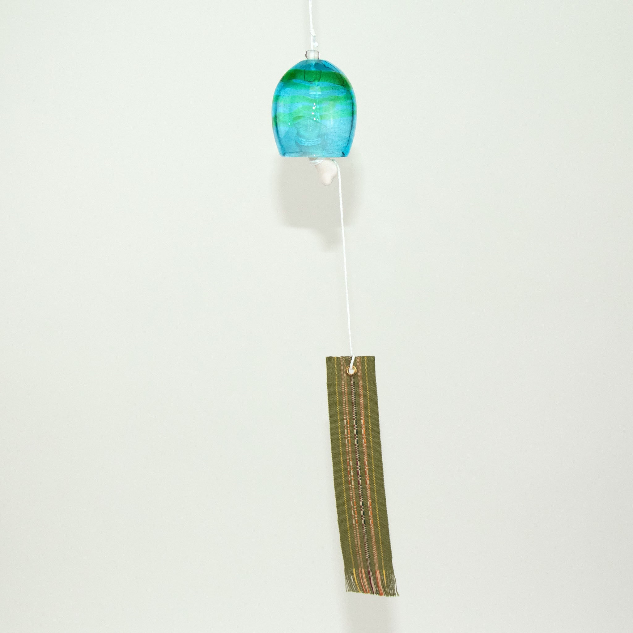  Blue glass Okinawan wind chime with green handwoven tab by Miyahira Studio, suspended on a white background.