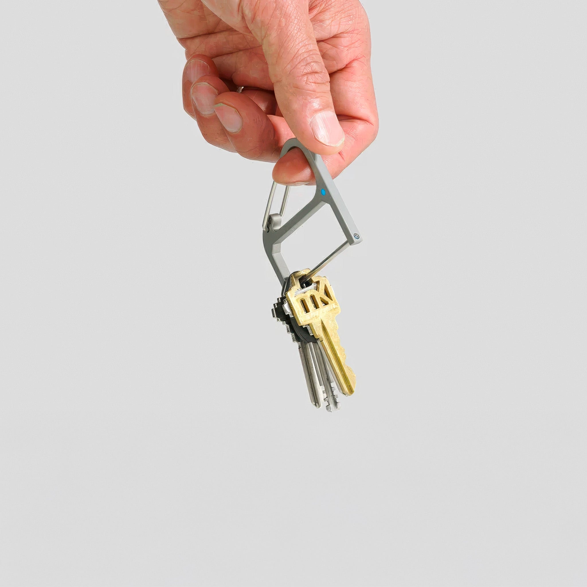 Hand holding CW&T's titanium key wrangler with keys against a light gray background