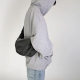 Person wearing a gray hoodie with hmhy's black buddy bag over one shoulder on a white background