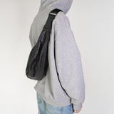 Person wearing a gray hoodie with hmhy's black buddy bag over one shoulder on a white background
