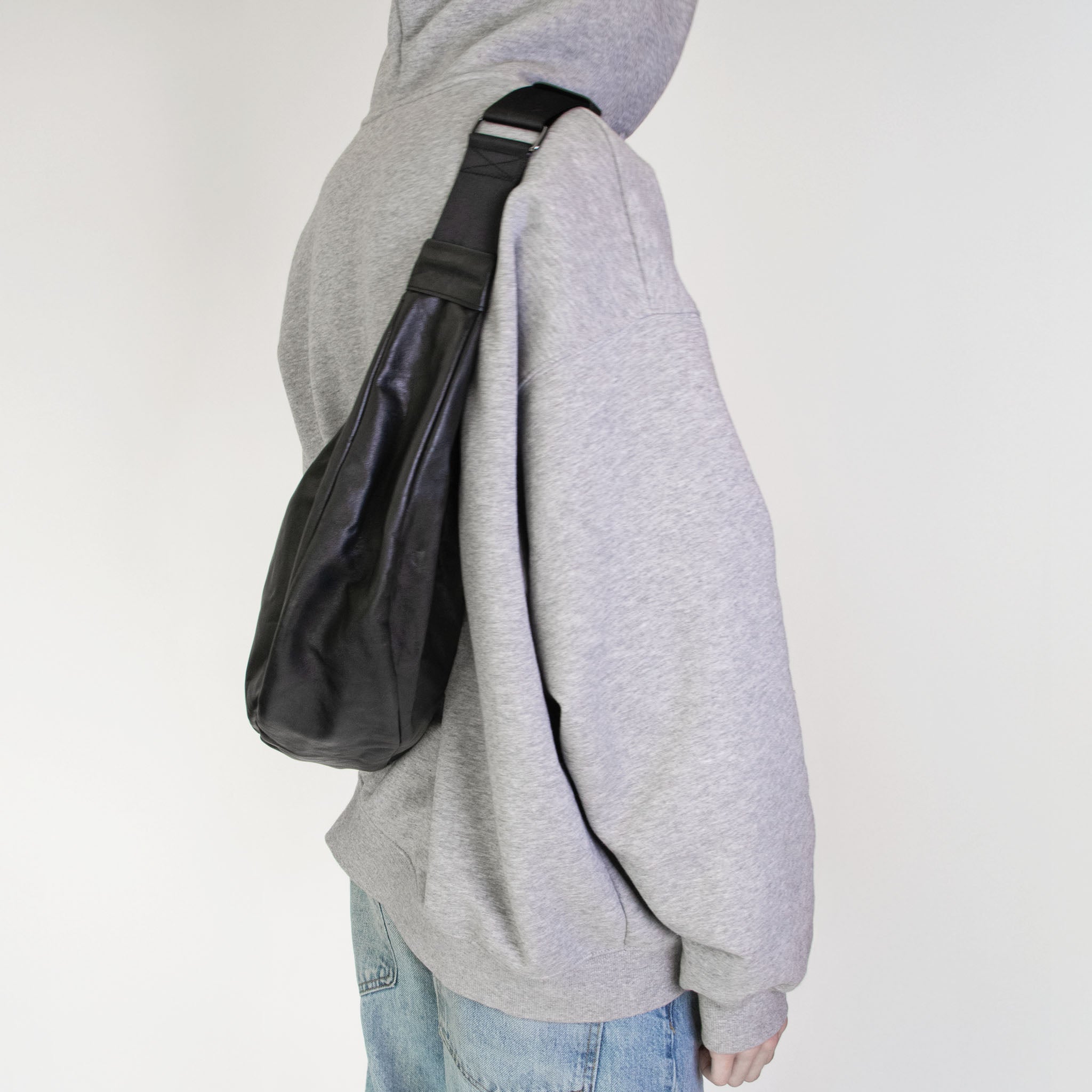 Person wearing a gray hoodie with hmhy's black buddy bag over one shoulder on a white background