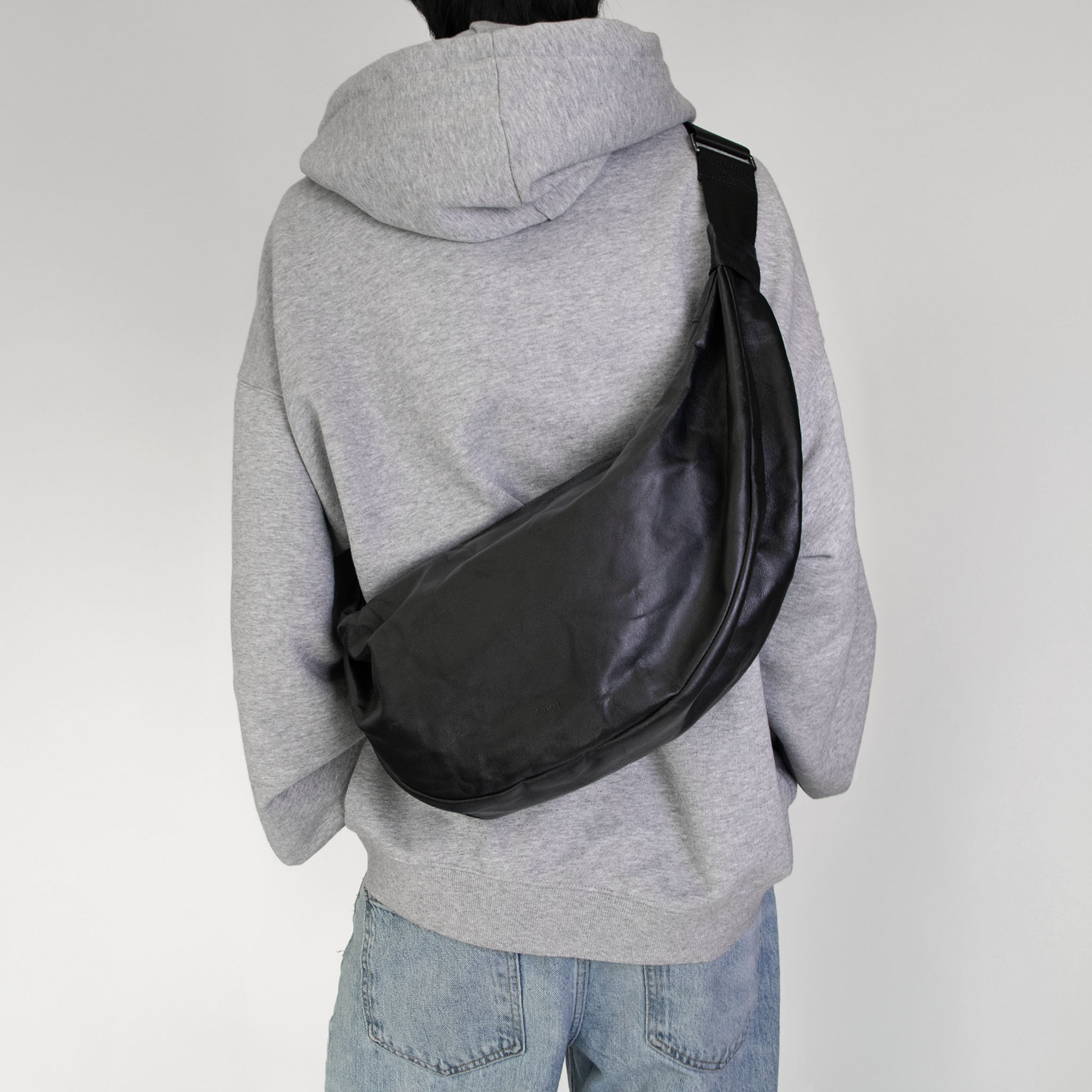 Person wearing a gray hoodie with hmhy's black buddy bag over one shoulder on a white background
