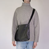 Person wearing a gray sweater and NImes black messenger bag on a plain background